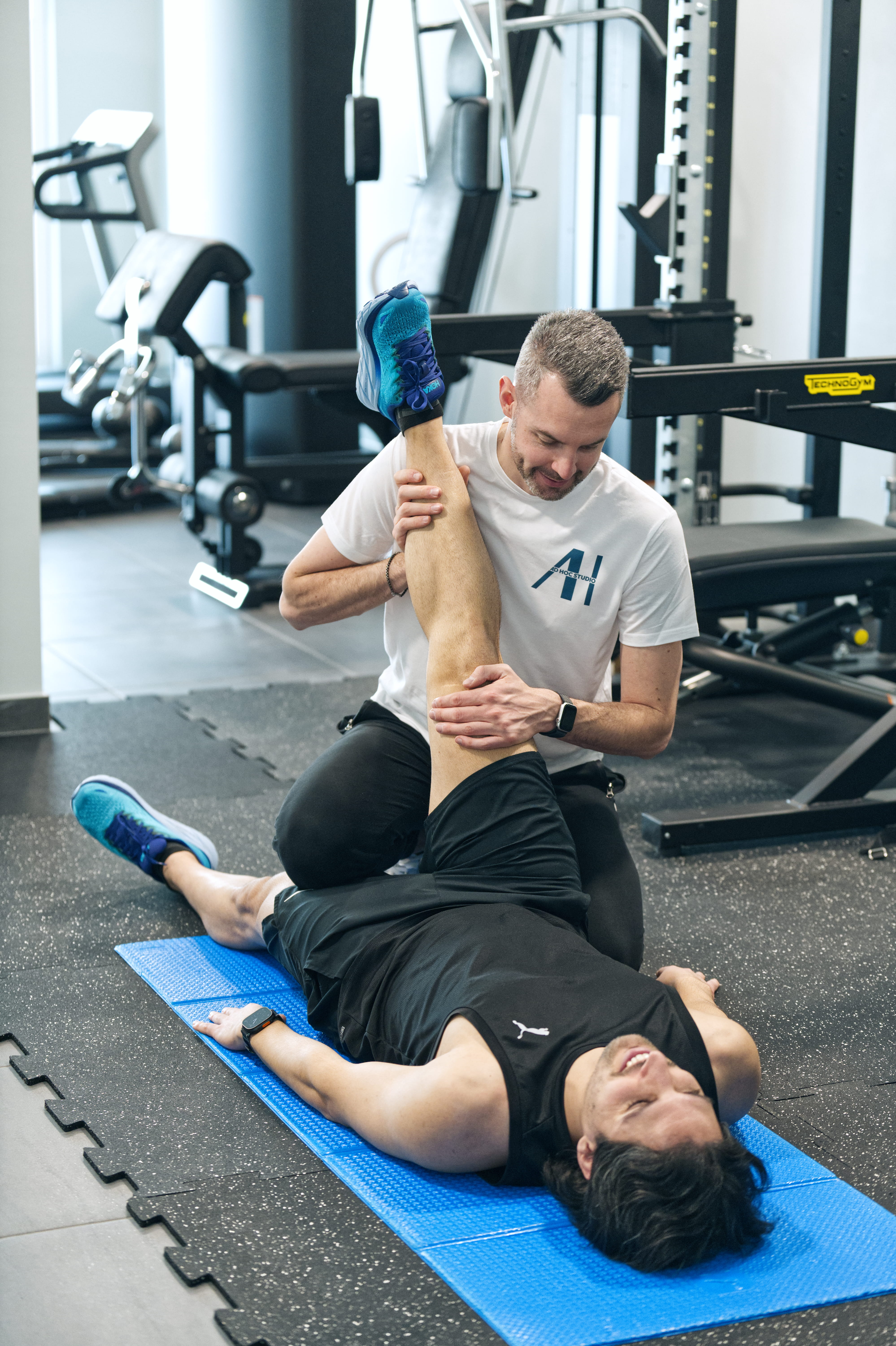 A man and woman sit on beige chairs in a modern room with a red paneled wall. A red pendant light hangs above a wooden coffee table between them.