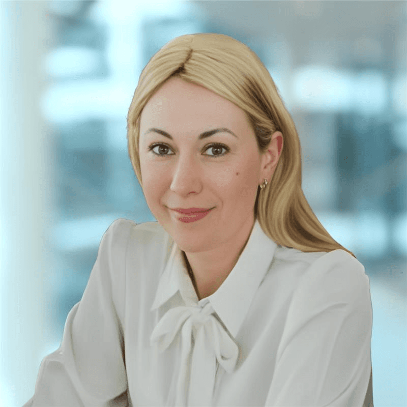 A smiling person wearing glasses and a patterned shirt stands against a plain white background.