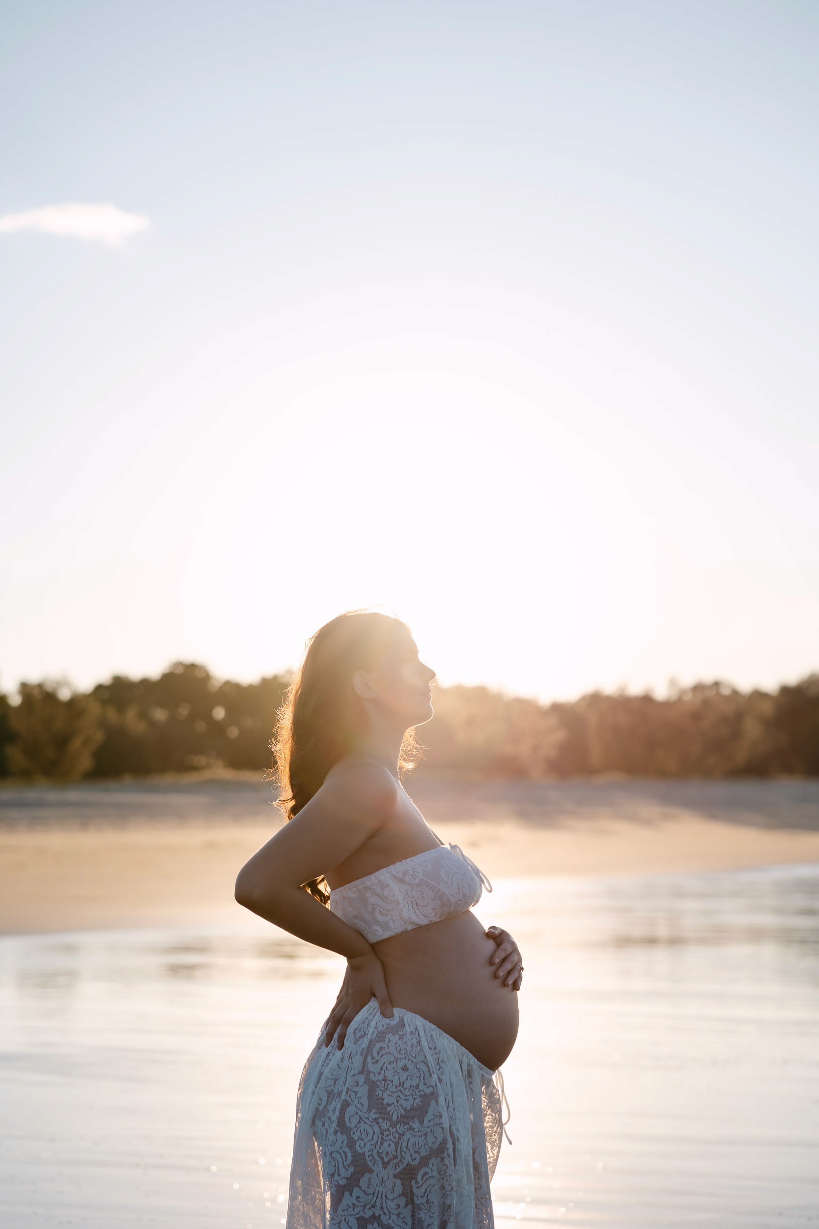 Glowing sun behind pregnant woman on the beach