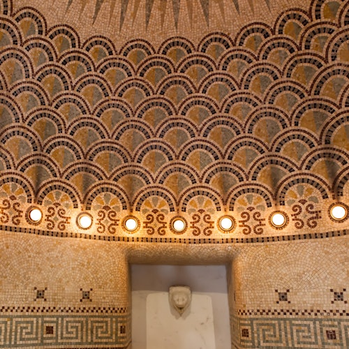 Intricate mosaic dome featuring a scallop pattern, illuminated with circular lights, and a white stone bust at the base.