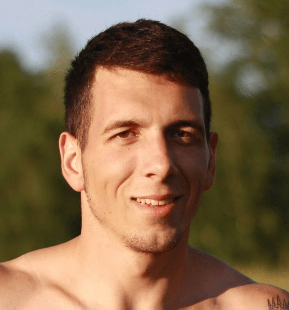 a shirtless man standing in a field with trees in the background