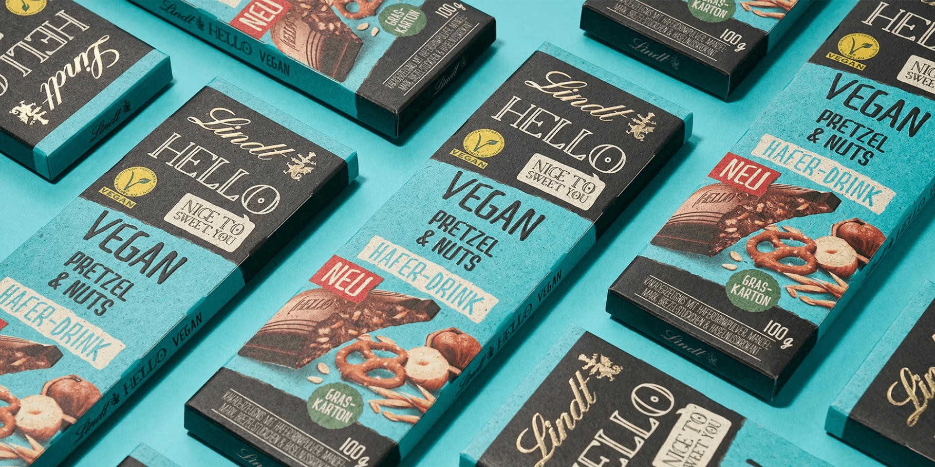 Markenwelt Lindt Hello Vegan – türkise Tafelschokoladen-Packung „Pretzel & Nuts, Hafer-Drink" im Raster angeordnet.