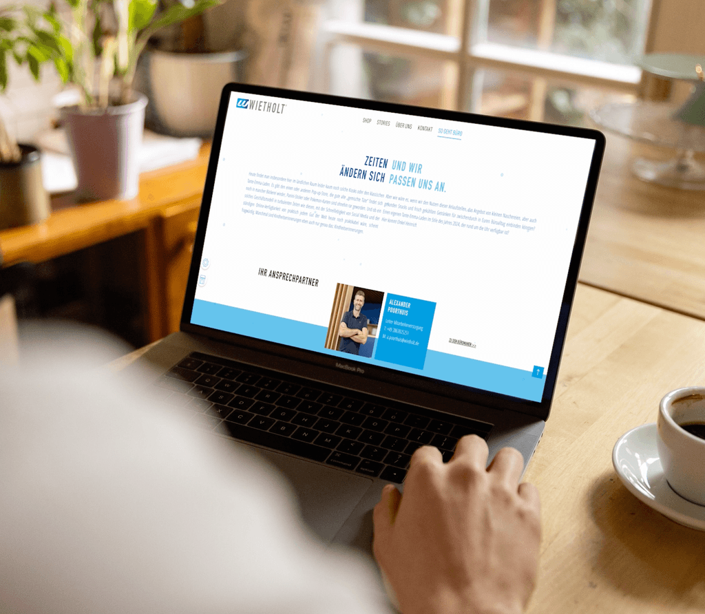 Ein mann sitzt in einem schönen Café an seinem Laptop und sieht sich gerade die Website der Firma Wietholt an während er seinen Kaffee genießt