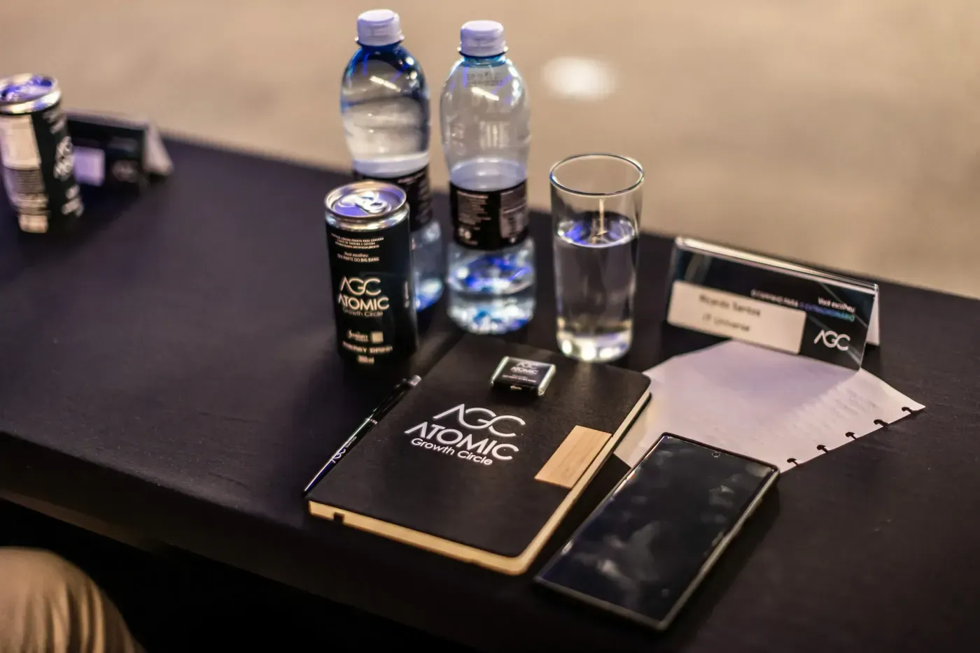 A table setting with two water bottles, a coffee cup, a notebook, and a pen arranged neatly. Atomic Growth Club. Atomic Group. Br24. 
