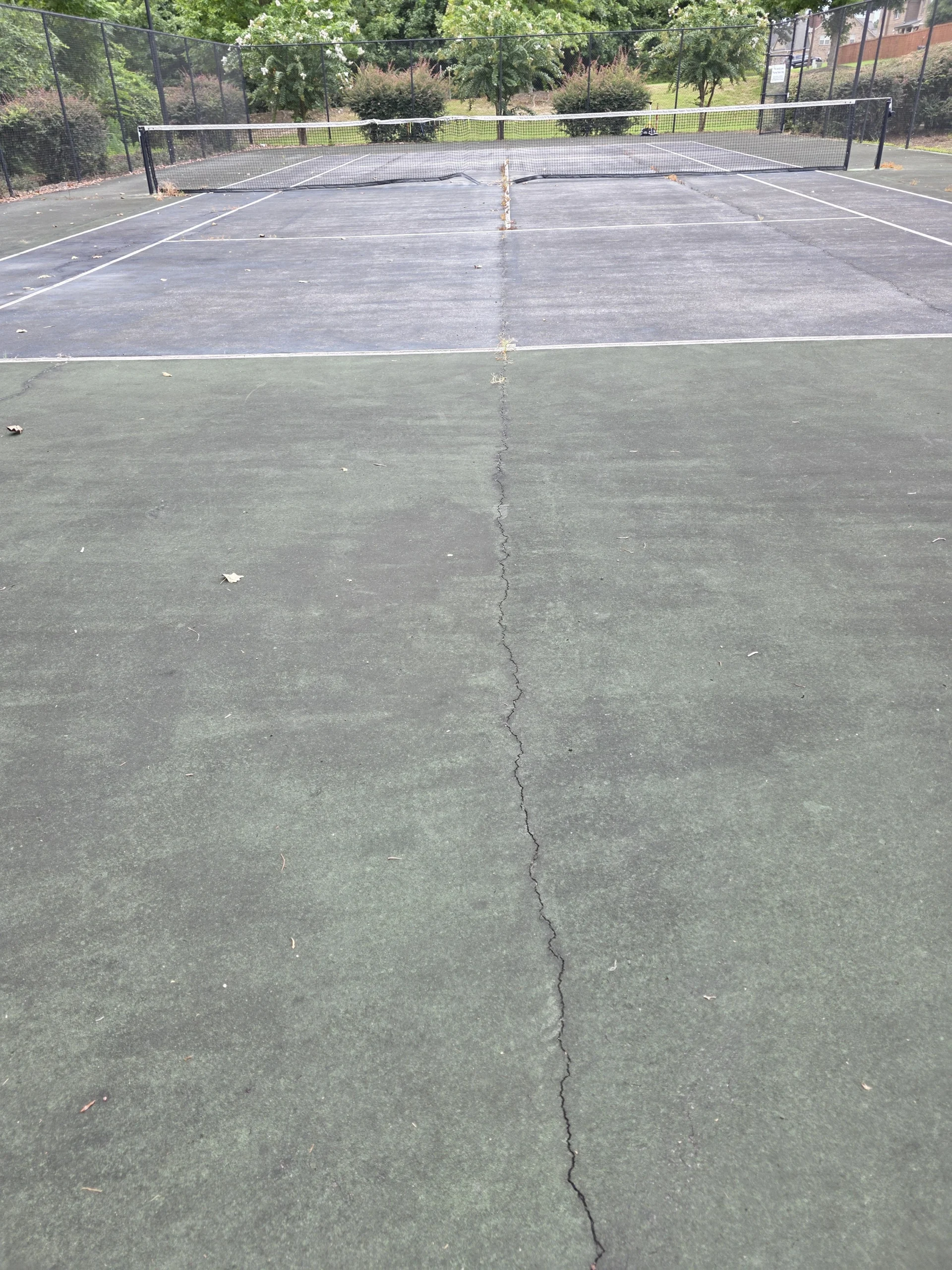 Faded HOA tennis court with visible center-line cracking before resurfacing in Fort Mitchell, AL