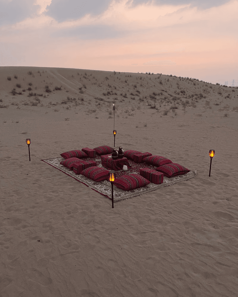 Single illuminated canvas tent glowing on desert sand at night beneath a clear, star-filled sky.