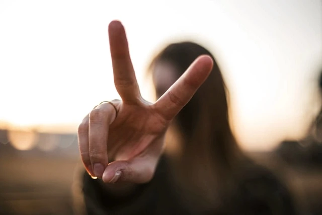 Closeup photo of a woman's hand giving the peace sign with a narrow depth of field so that the woman is blurry in the background