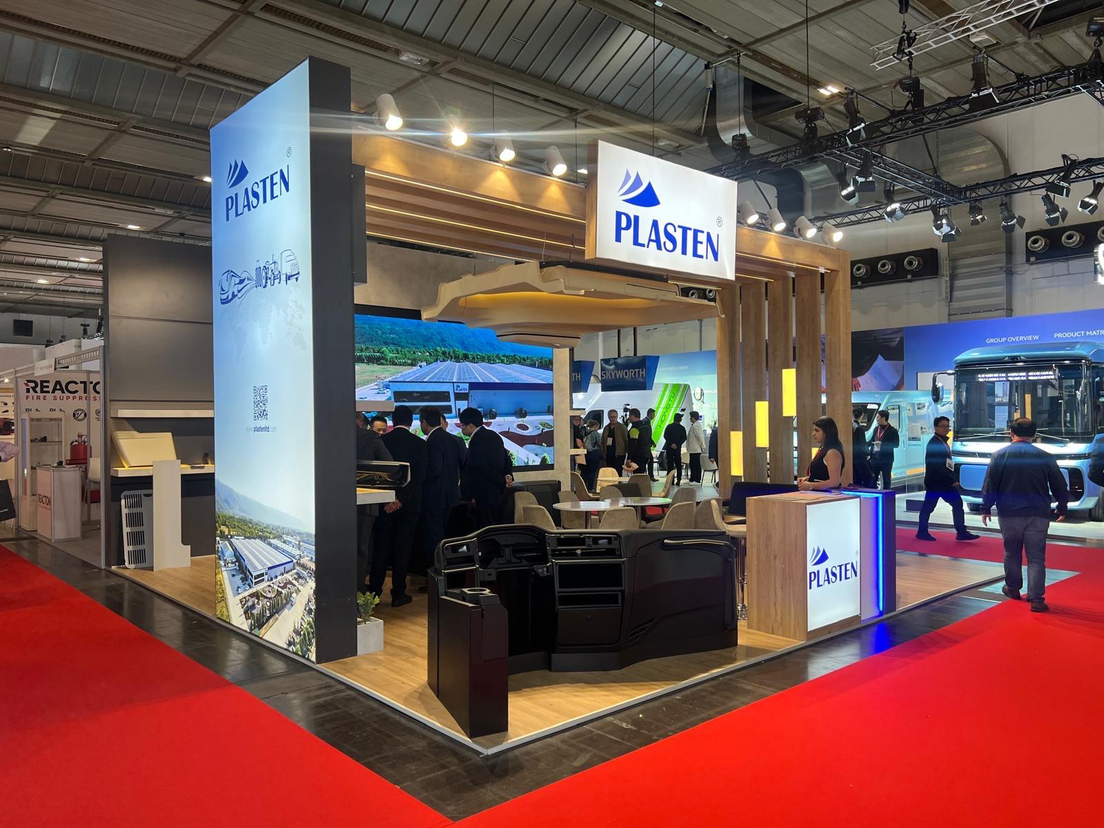 Plasten exhibition stand at Busworld 2025, featuring a warm wooden architectural frame, illuminated signage, and a clean professional layout.