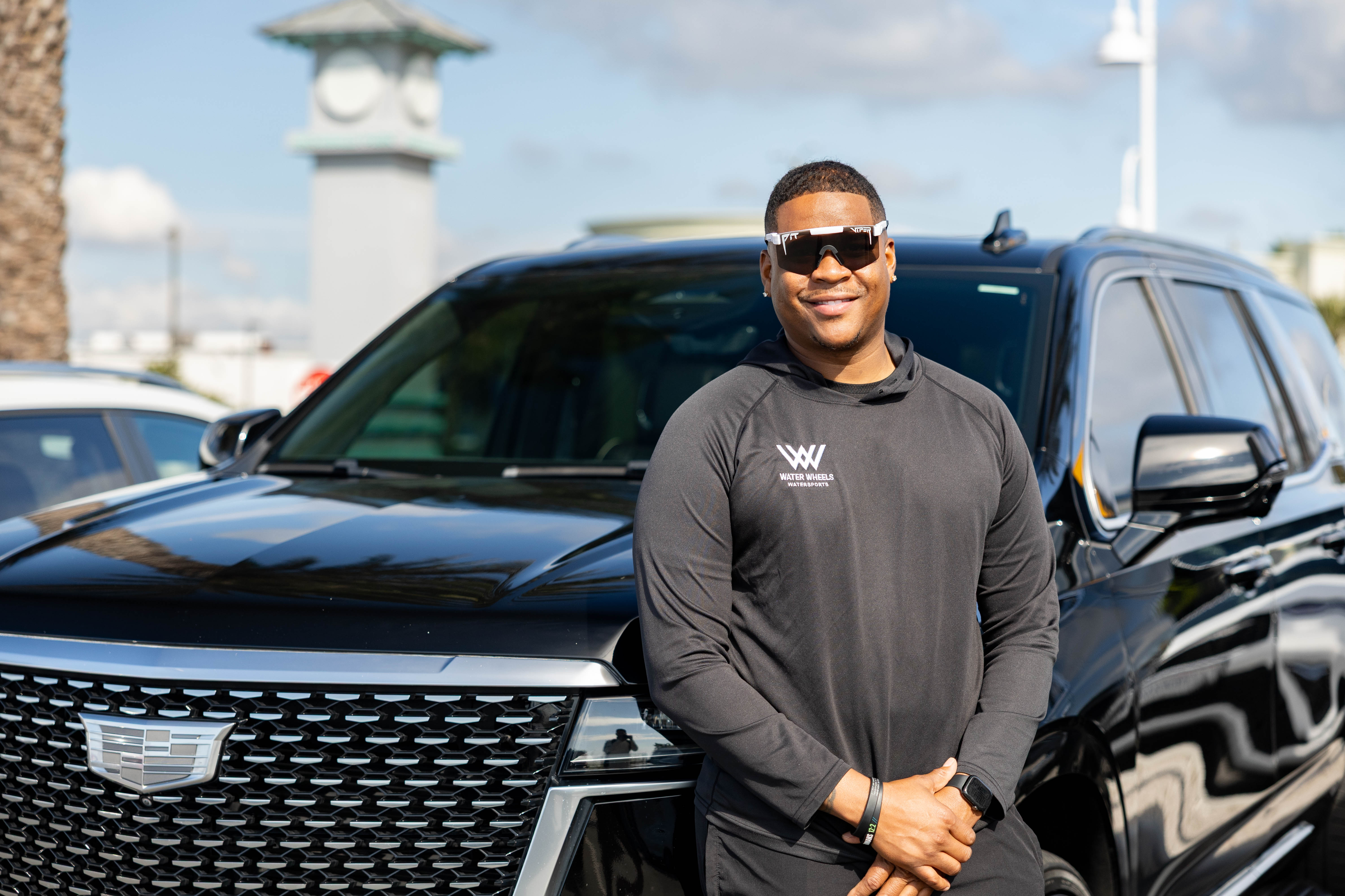 A group of six people gather around a wooden table where an older man in an apron kneads dough