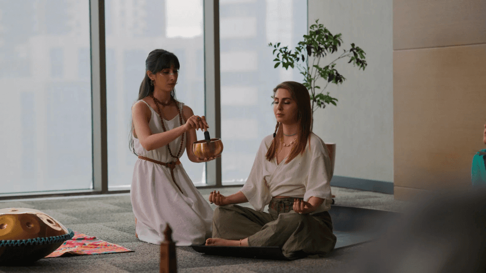 Two women are engaged in a meditation or wellness session as hypnotherapy inside a modern indoor space.