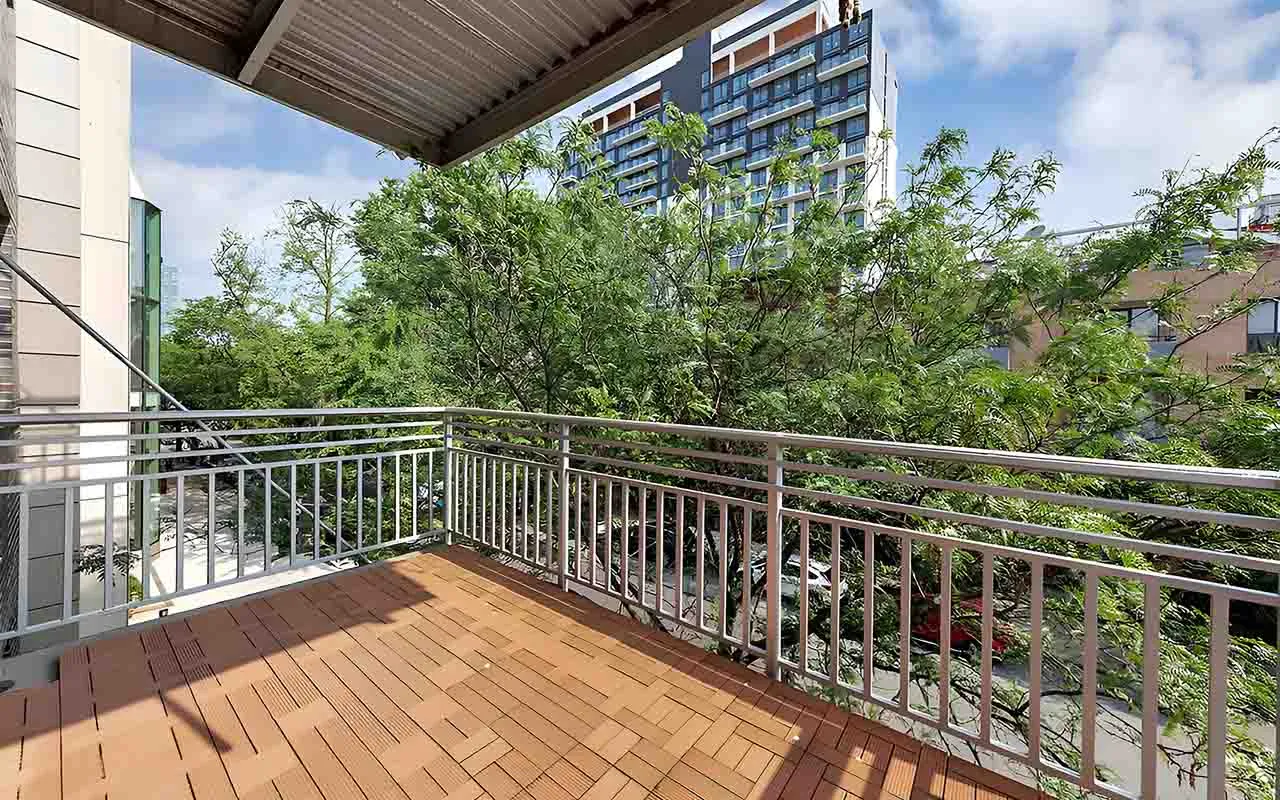 A balcony featuring wooden flooring and railing, providing a view of surrounding trees.