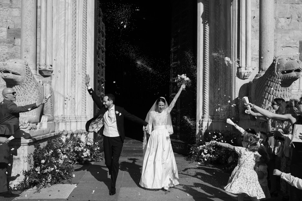 Sposi escono dalla chiesa con le braccia alzate, circondati da amici e familiari, momento di gioia matrimoniale