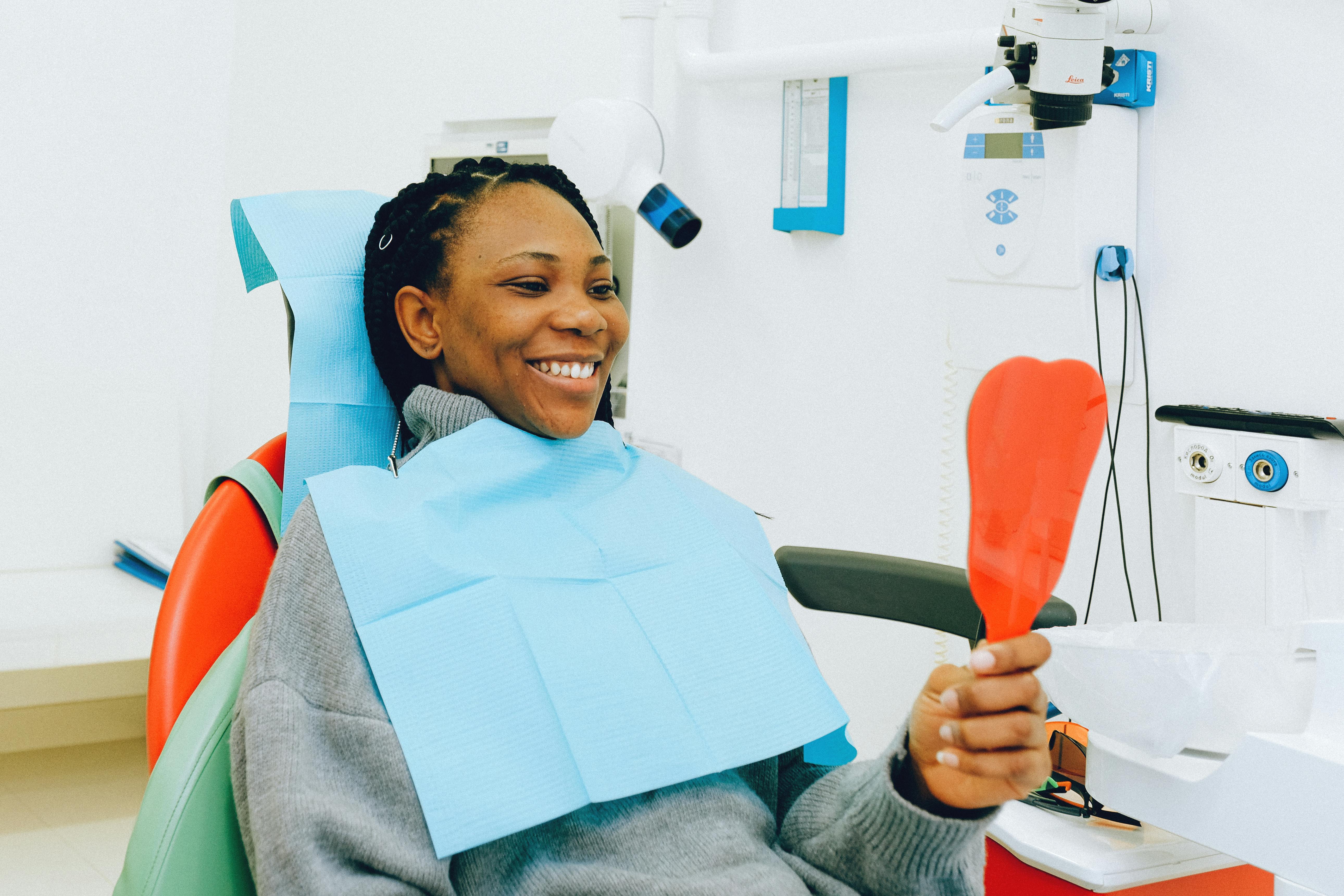 woman sitting in dental chair smiling at reflection in hand-held mirror
