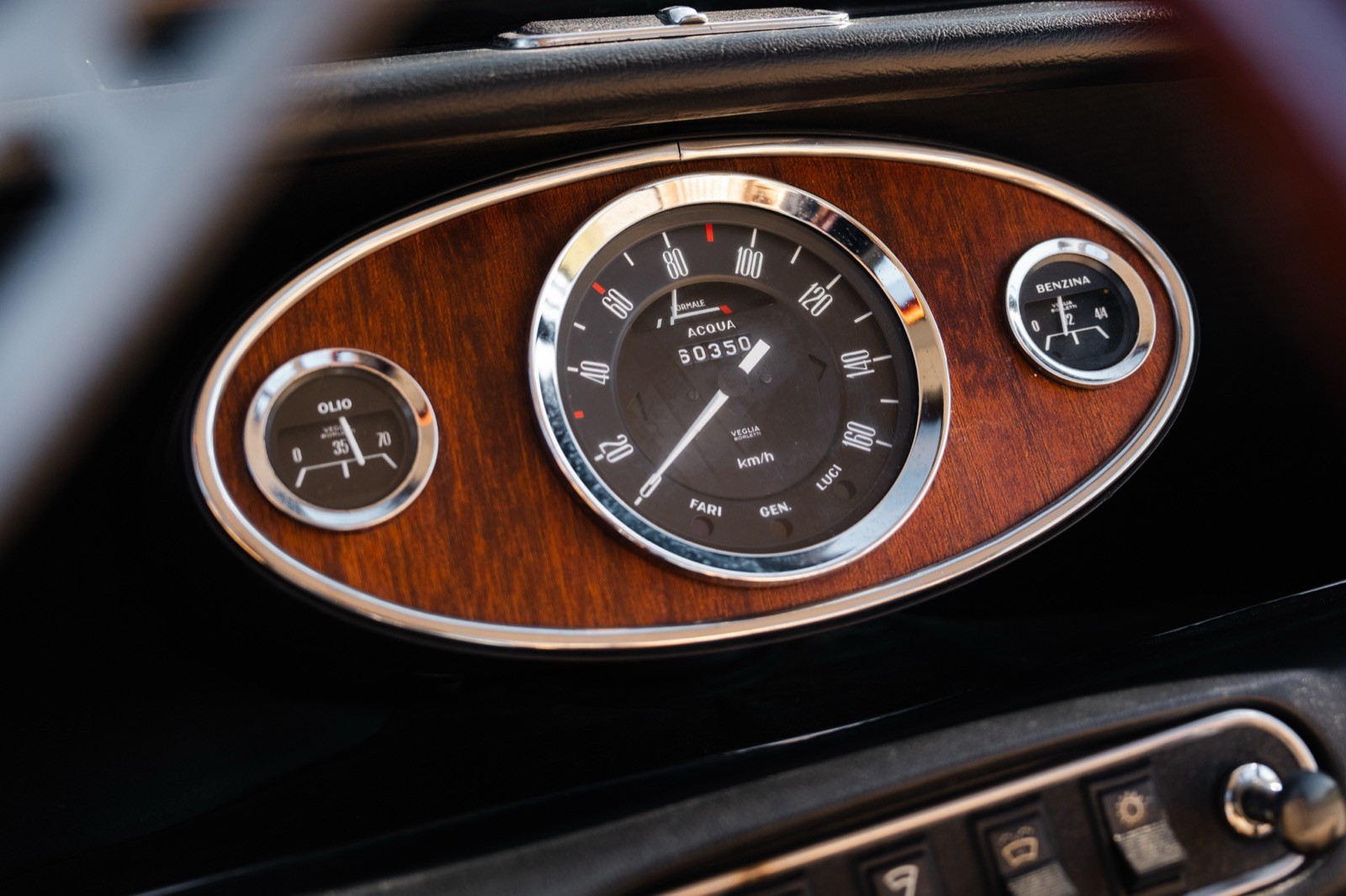 Close-up of a vintage car clock with a wooden panel background, featuring a round design and chrome accents.