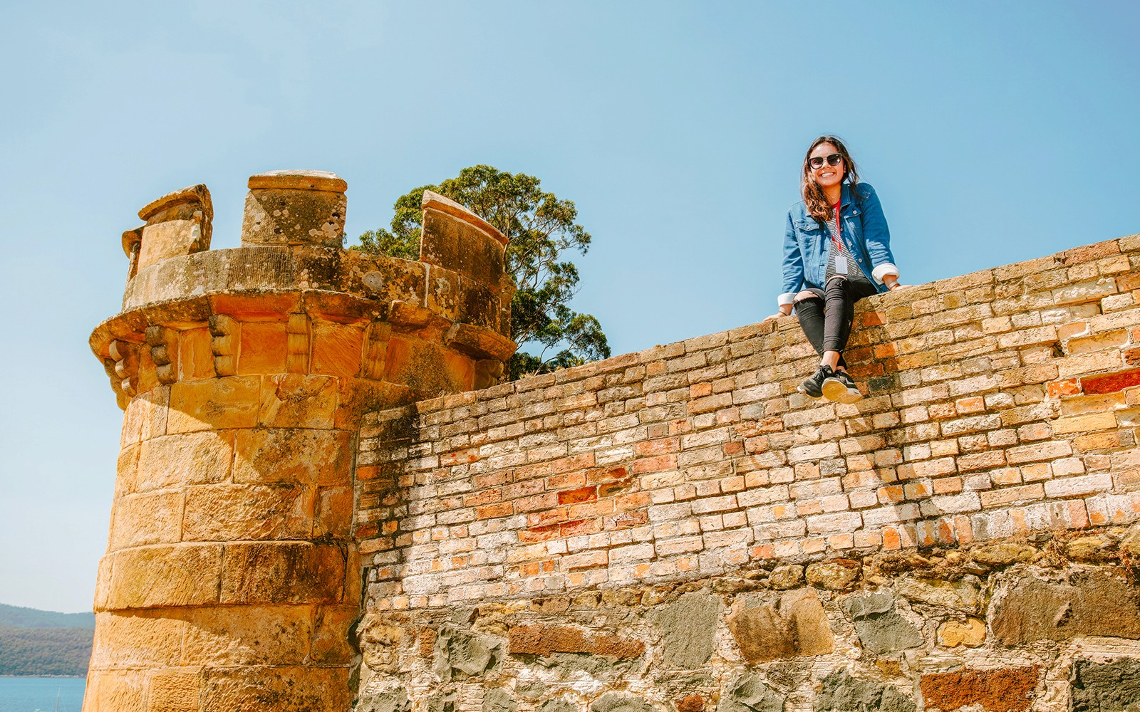 在塔斯马尼亚的亚瑟港，坐在历史悠久的石墙上的人，背景是美丽的风景。
