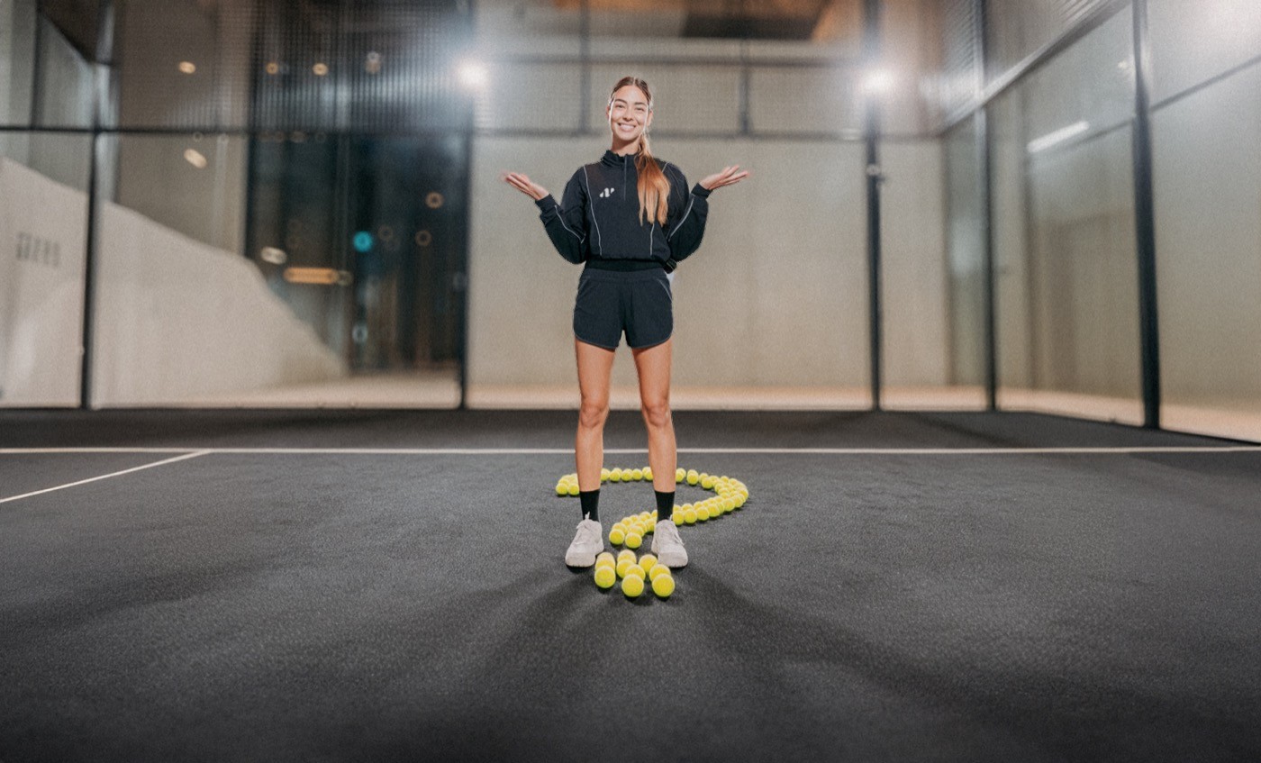 Padelspielerin steht lächelnd auf dem Court, umgeben von Bällen in Form eines Fragezeichens – ein spielerisches Motiv, das Neugier und Leichtigkeit bei Padelnero ausdrückt.