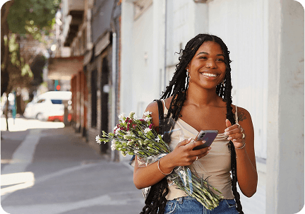 A person walking down a street with a bunch of flowers and phone in hand with a big smile on their face