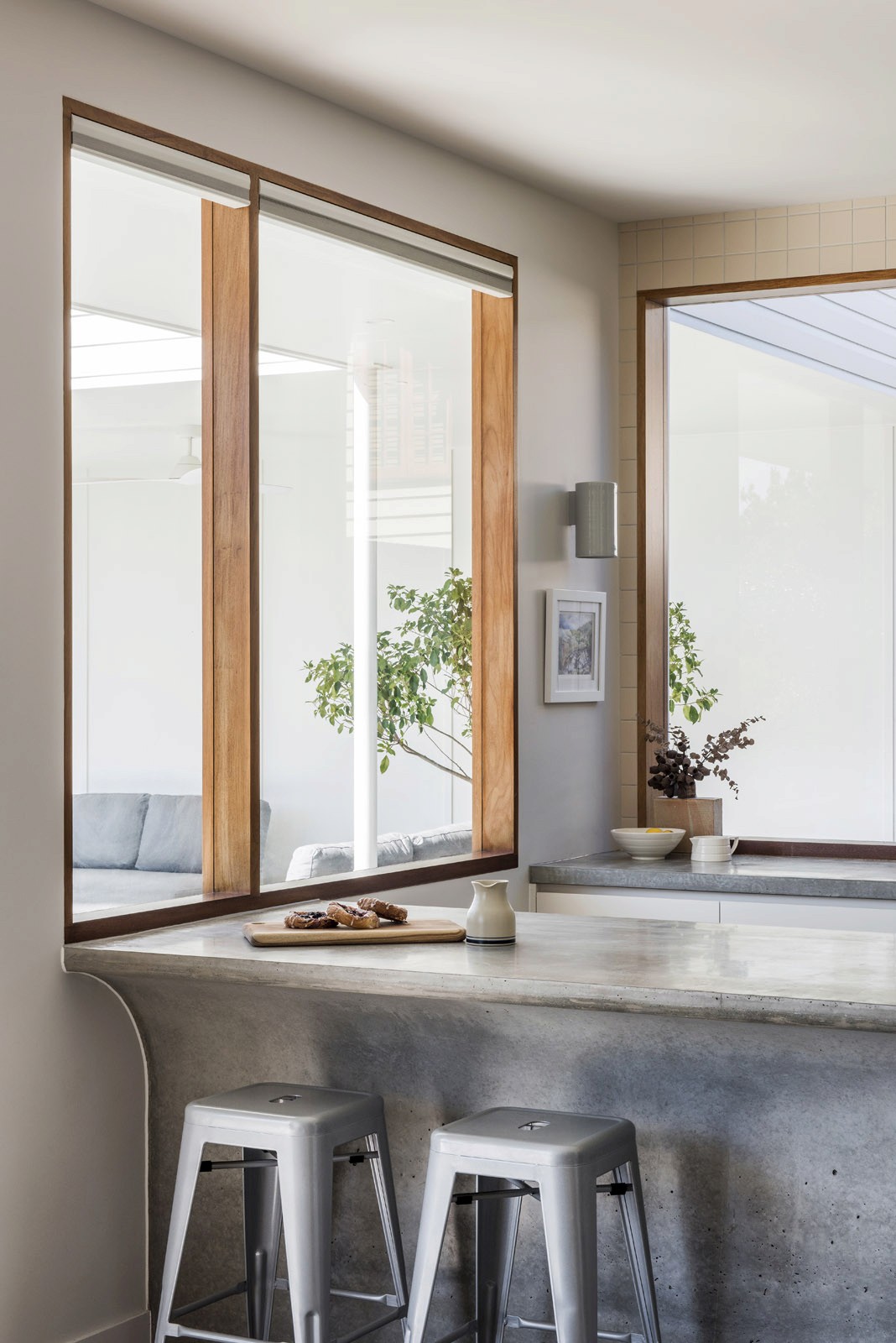 Kitchen bench with concrete countertop, timber-framed windows, and bar stools
