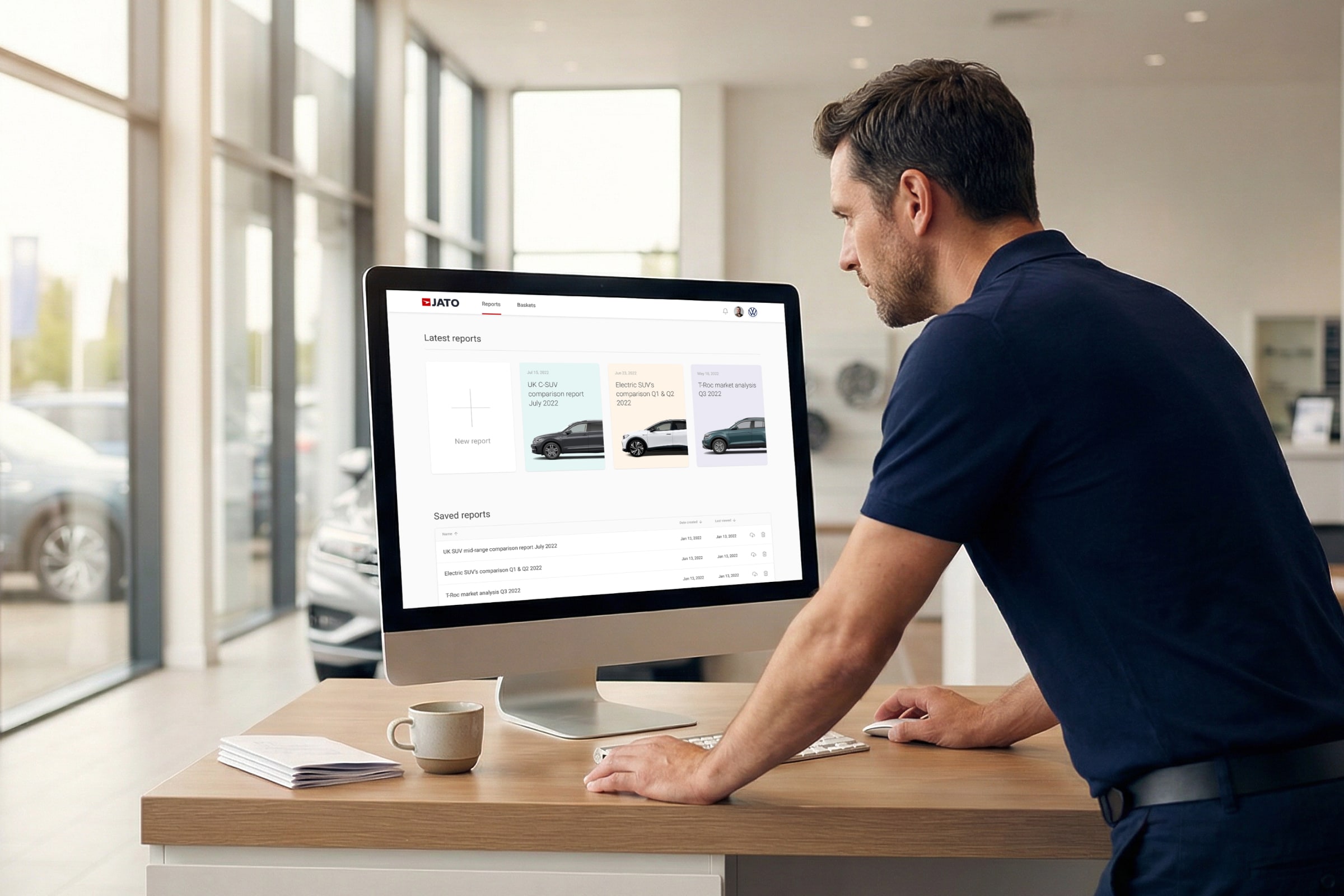 Car dealership professional viewing JATO reports dashboard on desktop monitor with showroom visible through windows behind