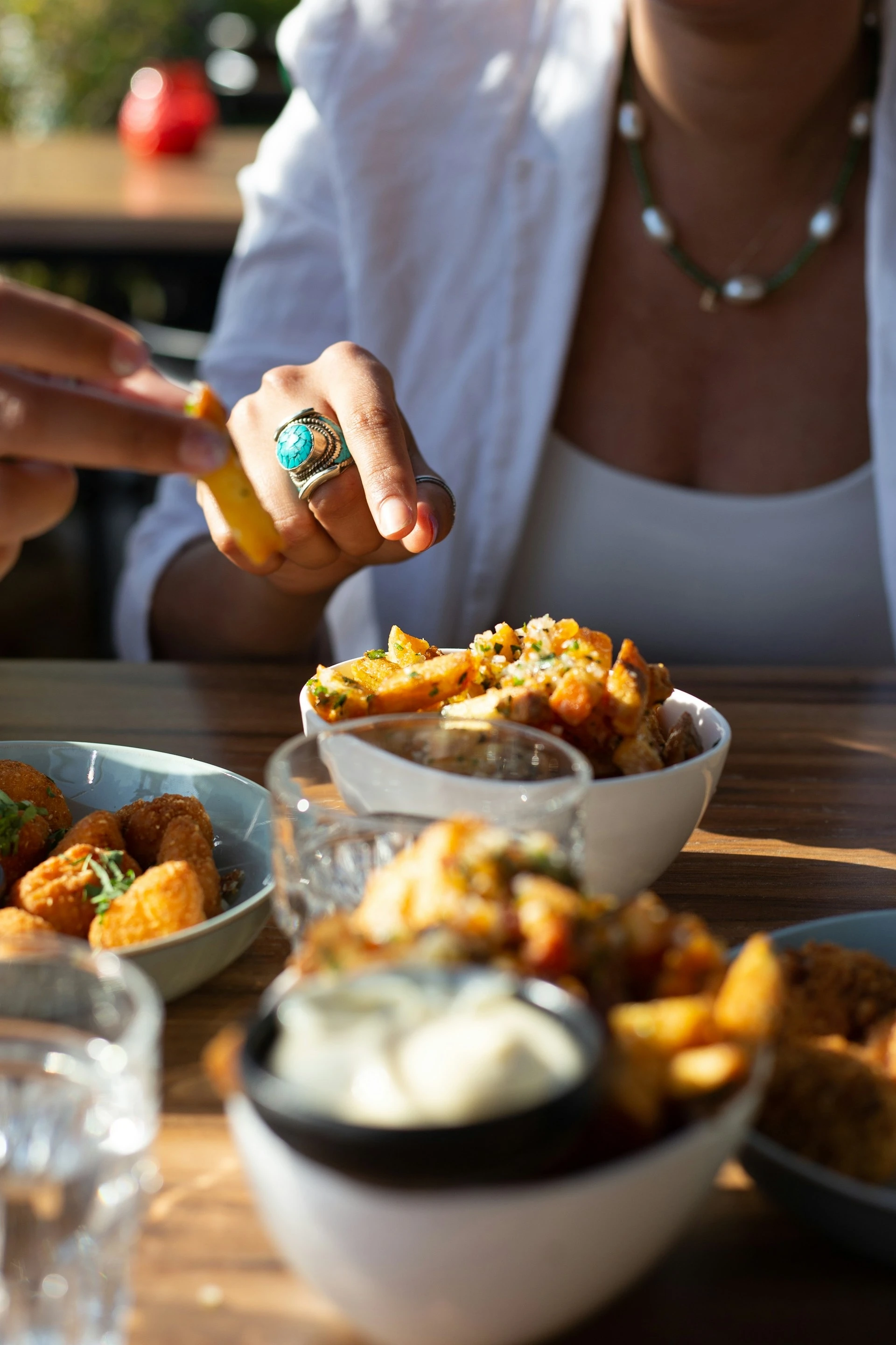 Gäste greifen an einem sonnigen Tisch zu Tapas und Beilagen