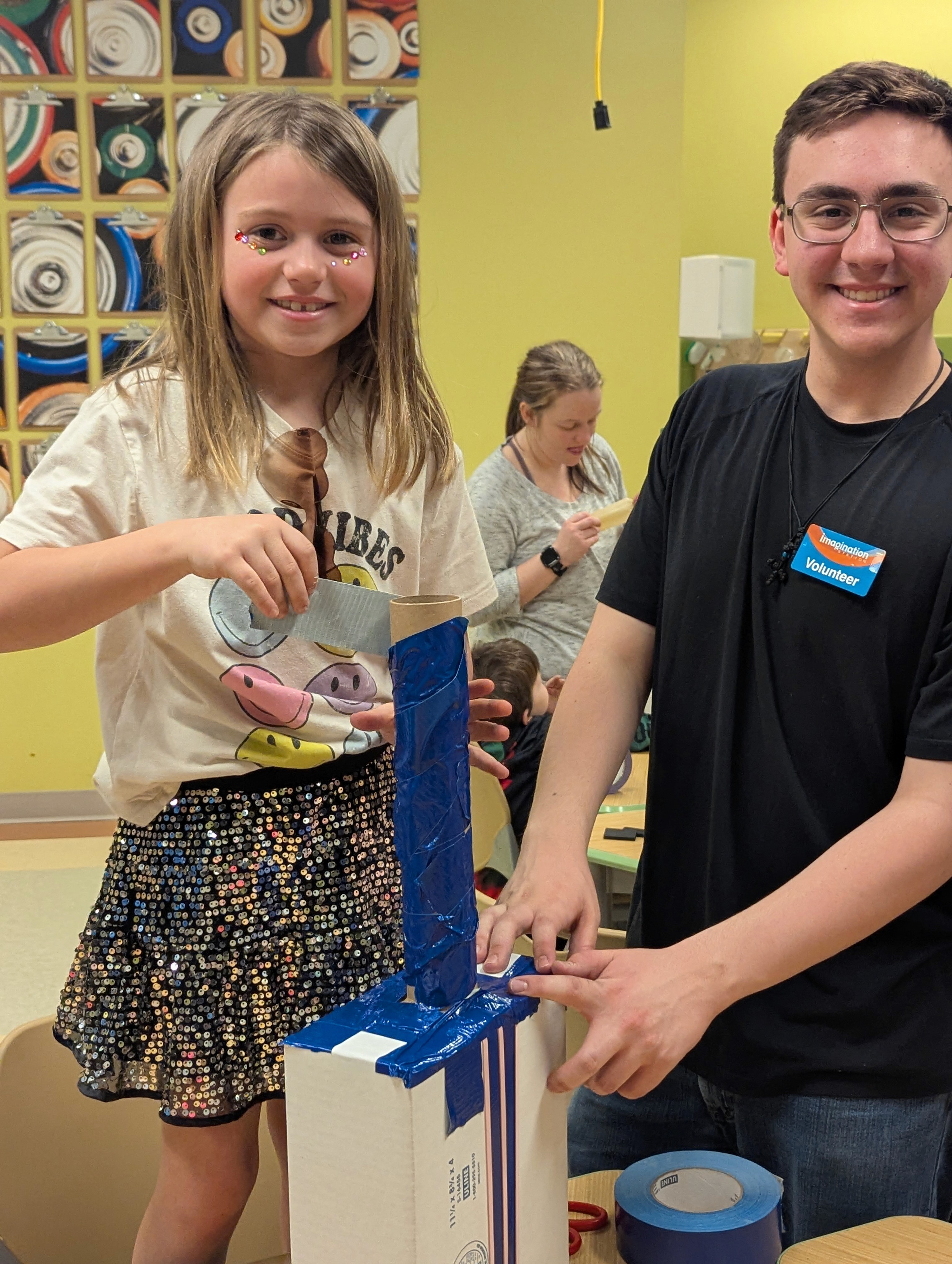A volunteer and girl work together to create a cardboard guitar.