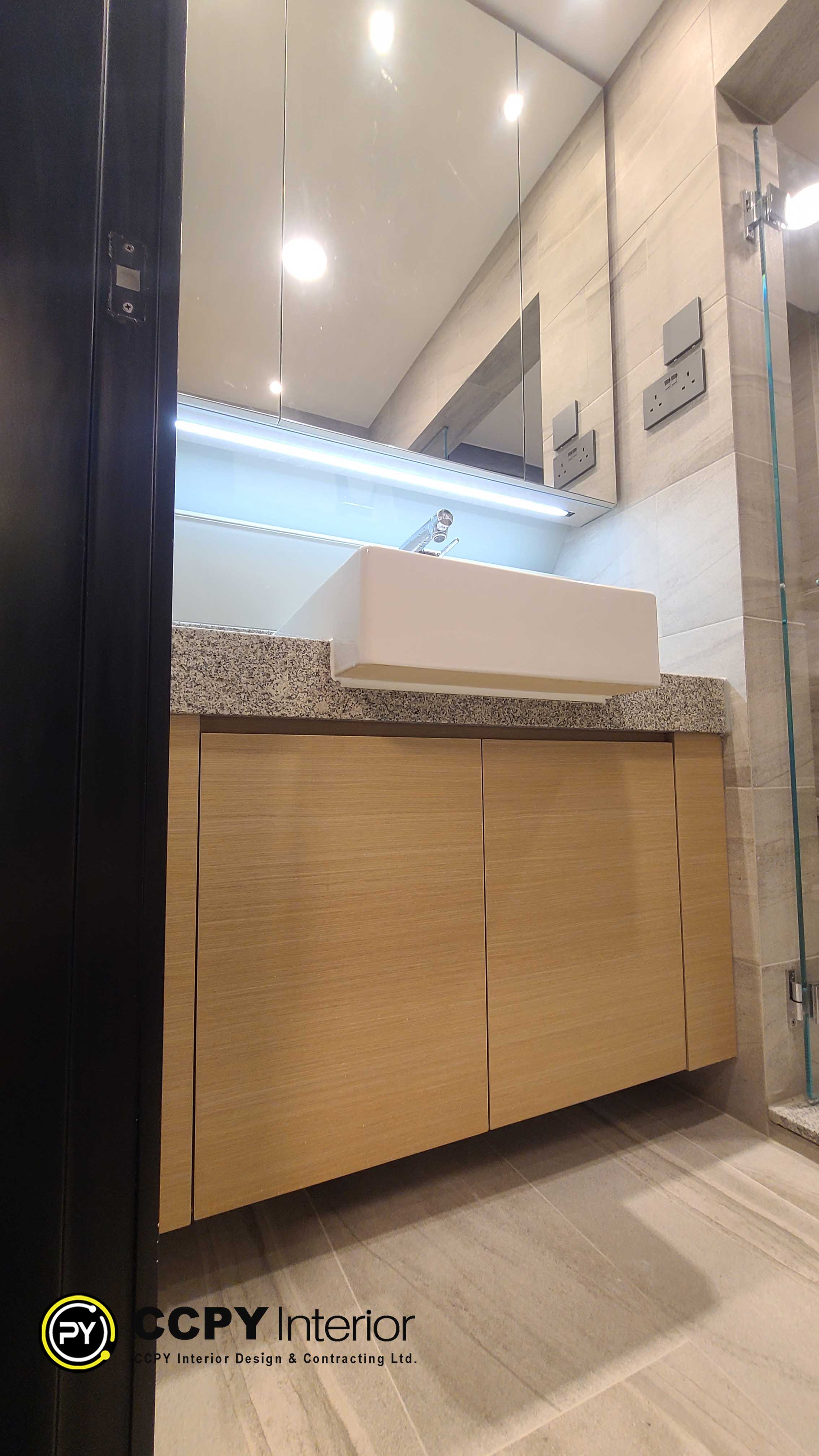 he selected region highlights a contemporary bathroom vanity unit featuring a rectangular vessel sink mounted on a speckled granite countertop. Below the countertop is a light wood veneer cabinet with integrated J-pull handles, framed by a dark architectural element on the left and neutral-toned wall tiles on the right.Key Design FeaturesVessel Sink: Crisp white, geometric rectangular washbasin sitting entirely above the counter line.Stone Countertop: Polished granite or engineered stone surface with a distinct grey and beige speckled pattern.Wood Cabinetry: Dual-door storage cabinet utilizing a warm, vertical-grain light wood veneer finish.Minimalist Hardware: Clean, handleless appearance achieved through integrated finger pulls at the top of the cabinet doors.
