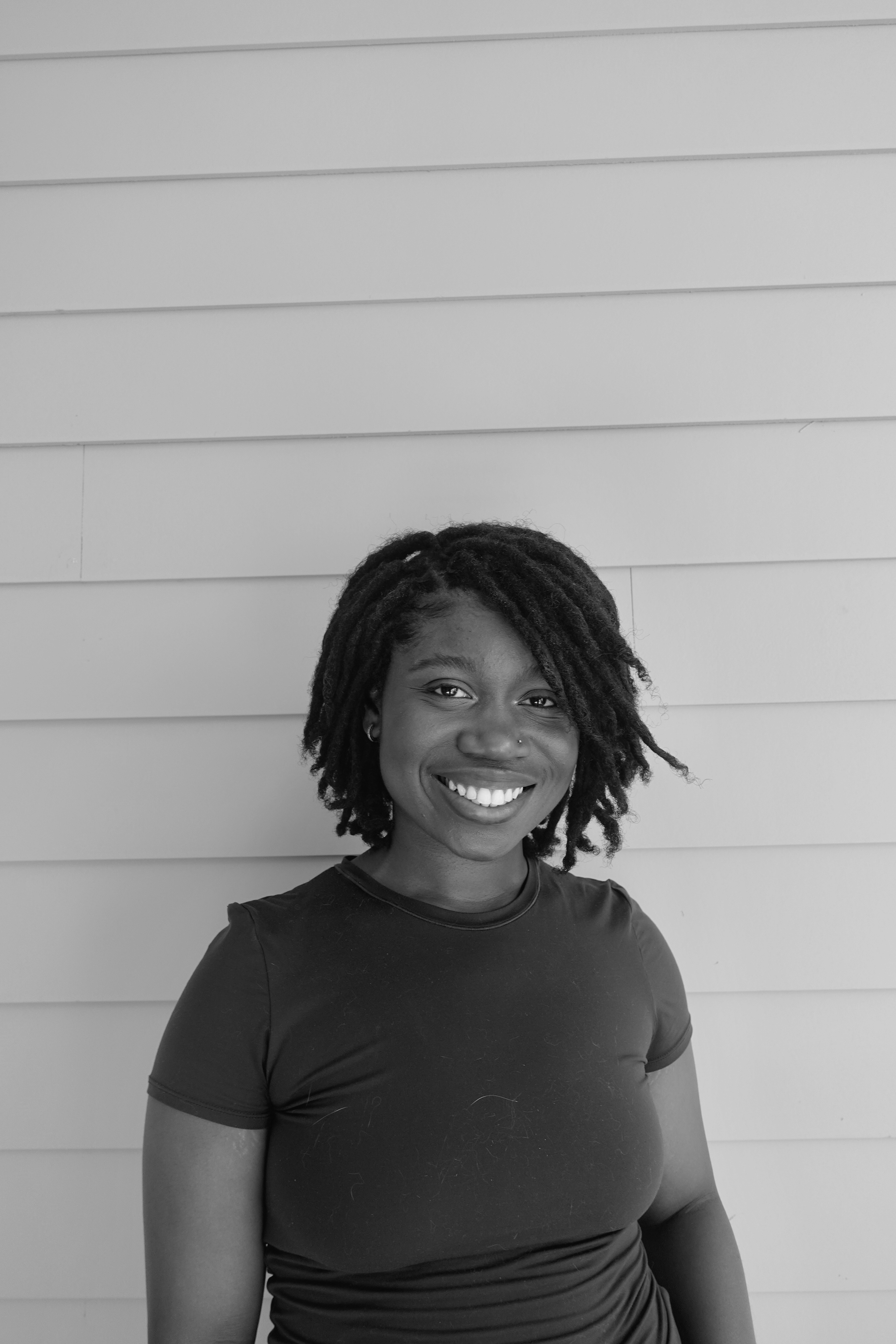 Person wearing a blue puffer jacket and red backpack standing in front of a light blue building on a city street.