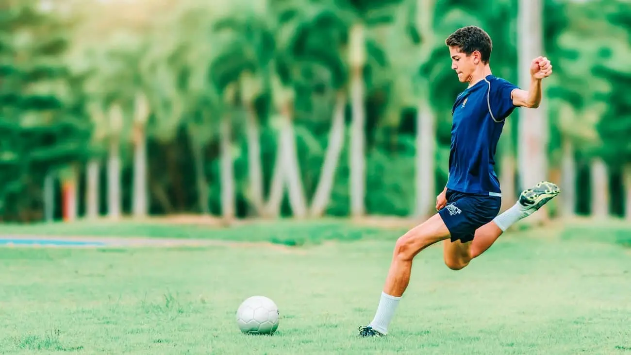 The image shows a young football player training on a green pitch, focussing on ball control and technique. This image lends itself perfectly to the theme of football training without pressure, underlined by the philosophy of Julian Nagelsmann, who emphasises the importance of freedom and creativity in football over negative pressure. The article discusses why excessive pressure in football is counterproductive and can affect the true enjoyment of the game as well as player performance.