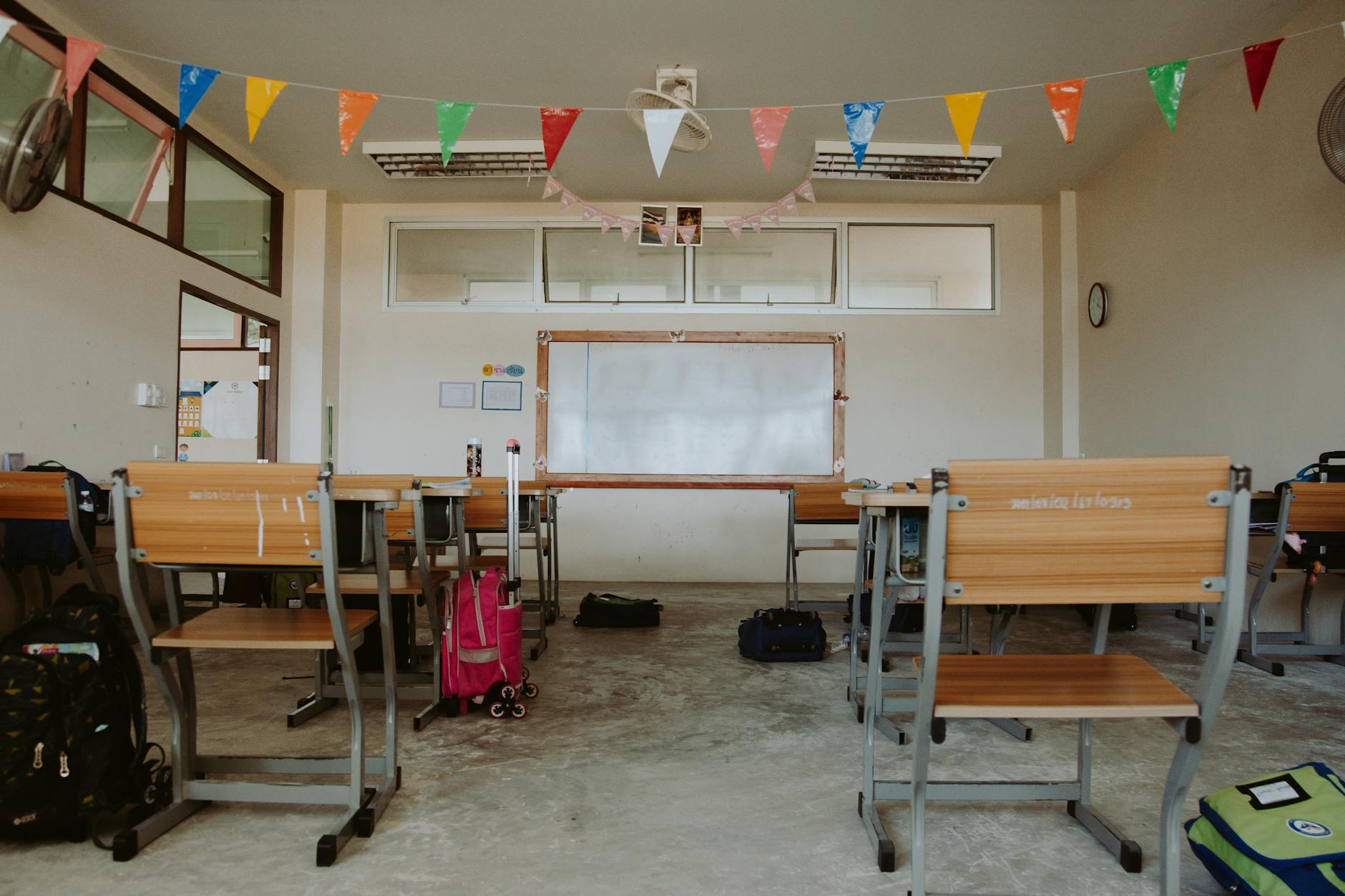 Sunlight streaming into a tidy classroom with chairs stacked and a daily schedule written on the board.