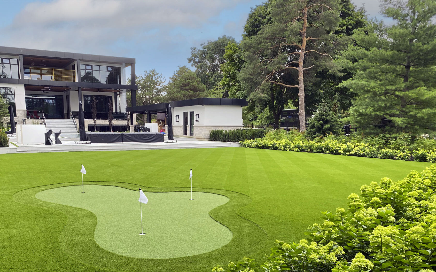 A large home in the background with a putting green in the foreground, enhanced by lush artificial turf from AGL Grass North.