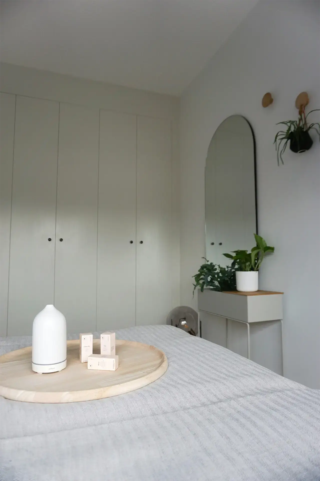 Nowoczesna sypialnia z minimalistyczną zabudową szaf wnękowych na wymiar, pokazana ze stylowymi dodatkami, takimi jak dyfuzor i lustro.