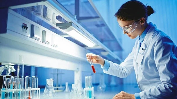 High school students exploring STEM through RISE Research summer programs, shown by a female scientist examining a test tube in a bright laboratory.