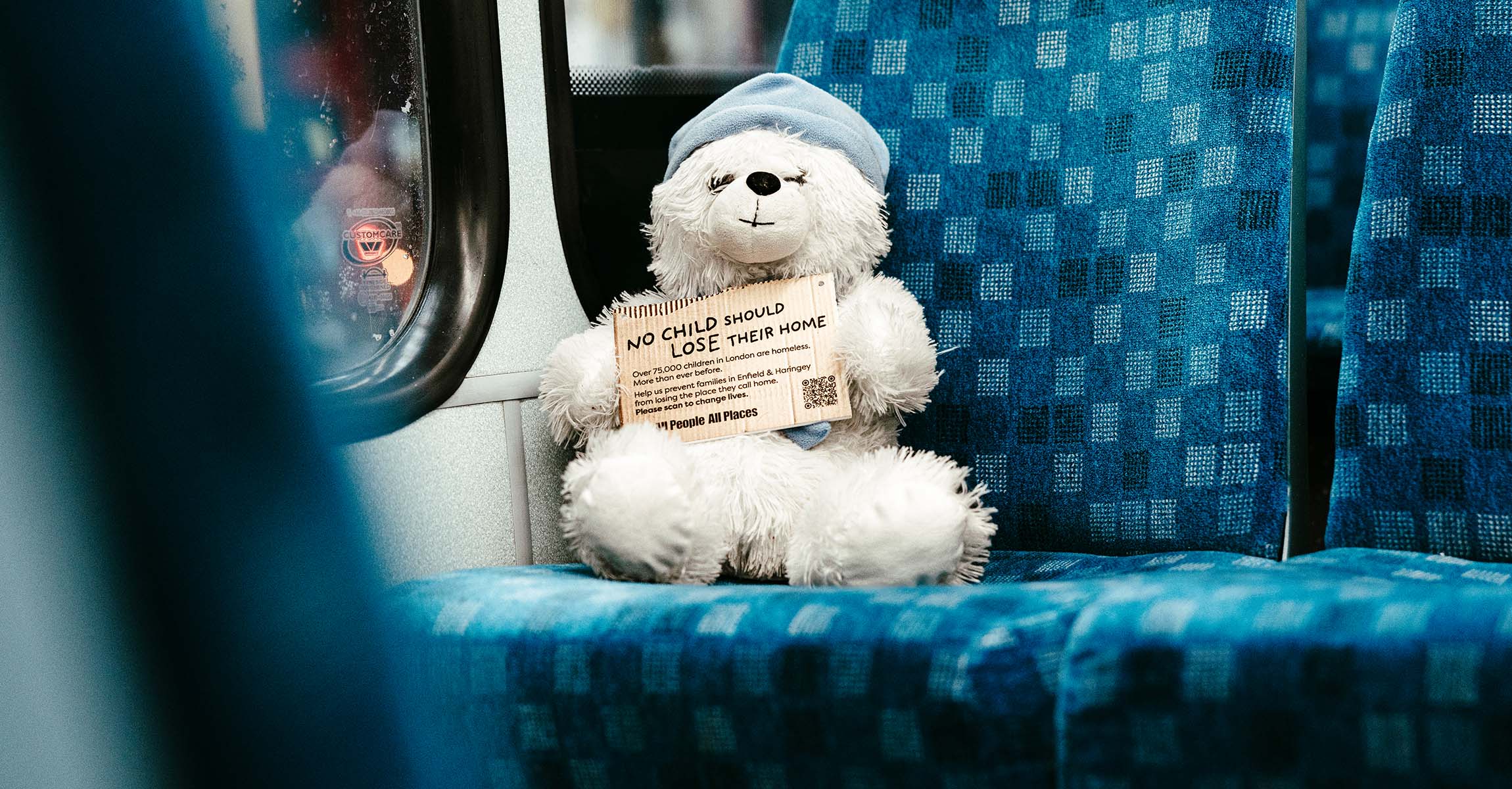 Stuffed white bear toy on an empty bus seatholding a sign that says No Child should loose their home