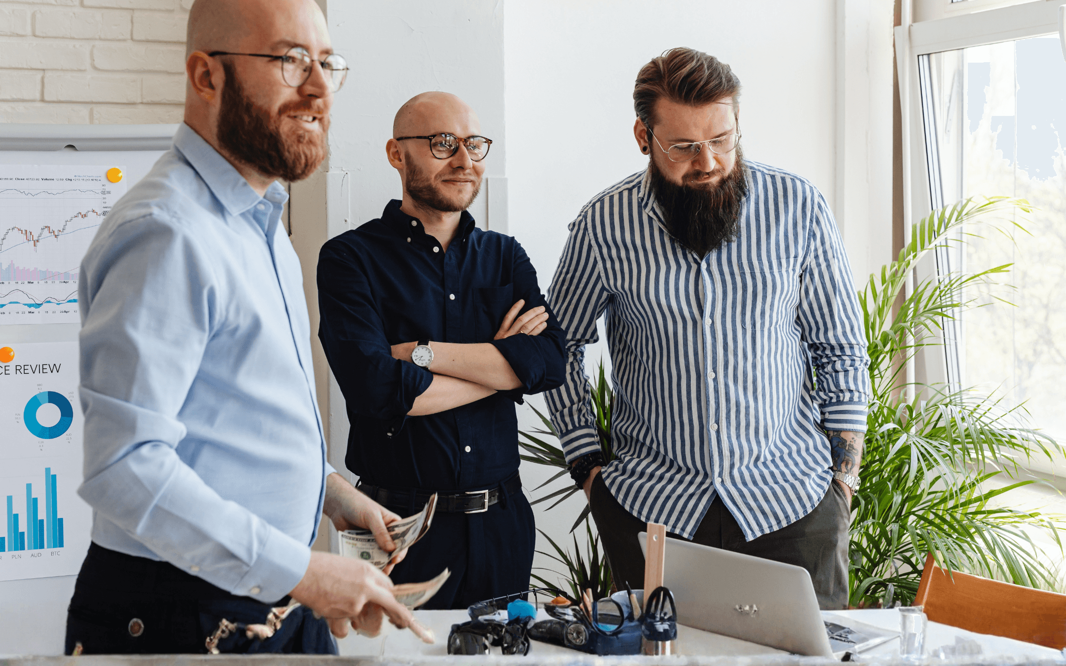Three men in a business meeting, looking at a laptop and documents on the table. Team discussing a project.