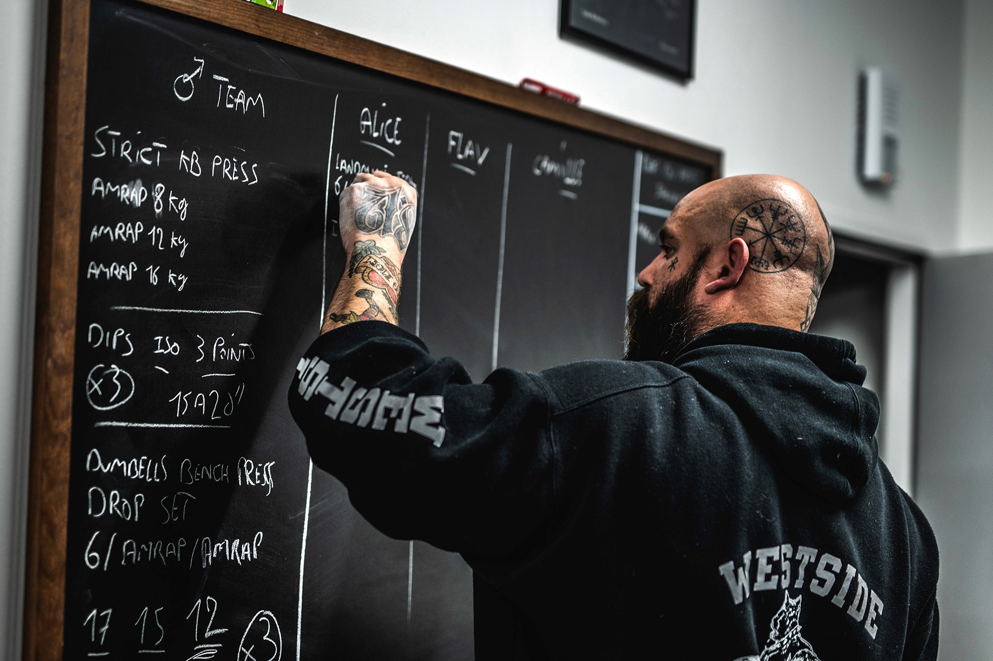 Two individuals are working out in a gym, focusing on dumbbells and strength training equipment.