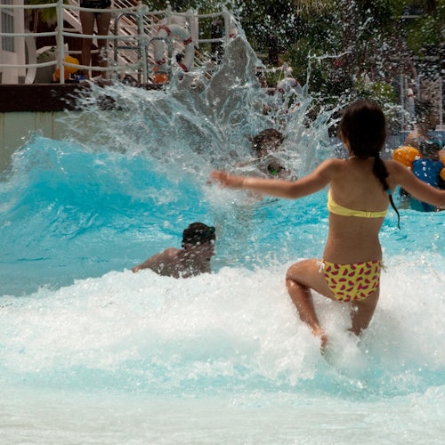 Children playing and splashing in a wave pool on a sunny day.