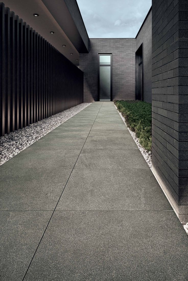 مسار خارجي لفيلا مودرن مكسو بحجر البازلت الممسوح ذو اللون الرمادي الداكن، يبرز التباين المعماري مع الجدران وحواف الزلط الأبيض.