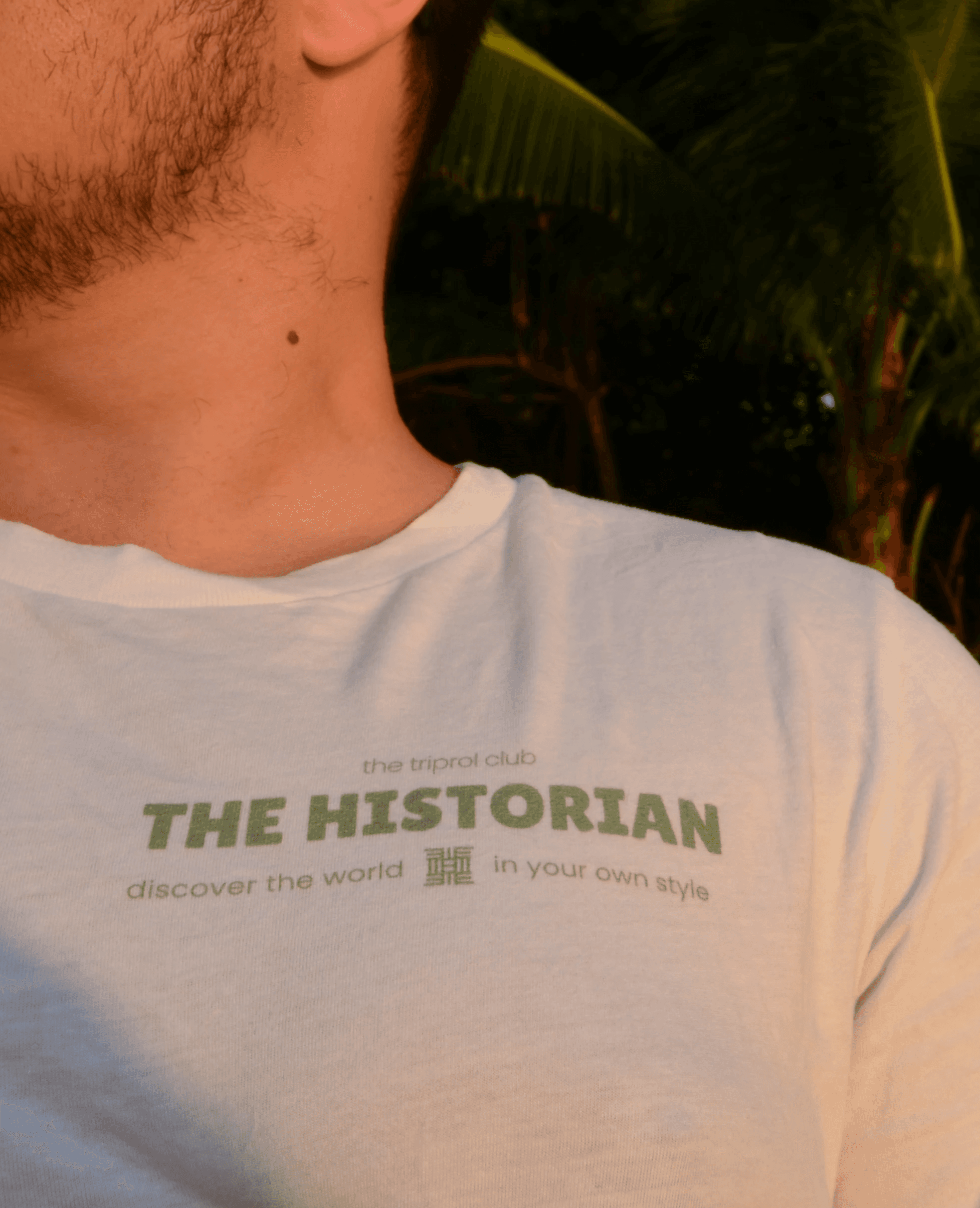 Smiling young woman with long hair standing against a dark green background, holding a finger to her chin.