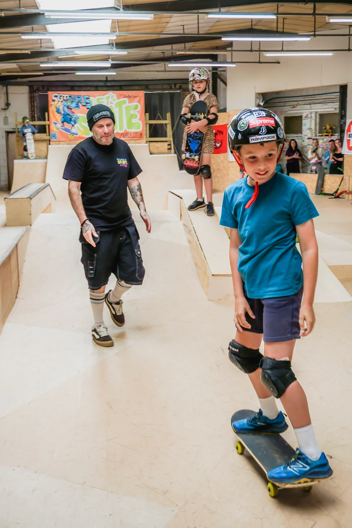 A young skater holding a skateboard in front of the Skate Farm mural at the indoor skatepark in Haywards Heath, Sussex