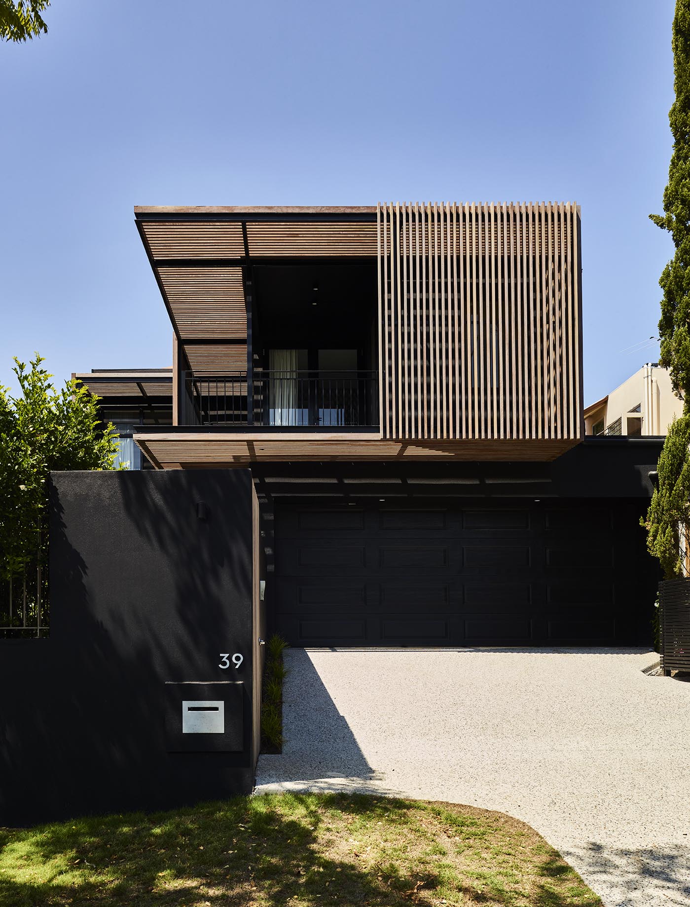 Modern two-storey home with timber slatted facade, black garage door, and minimalist front yard.