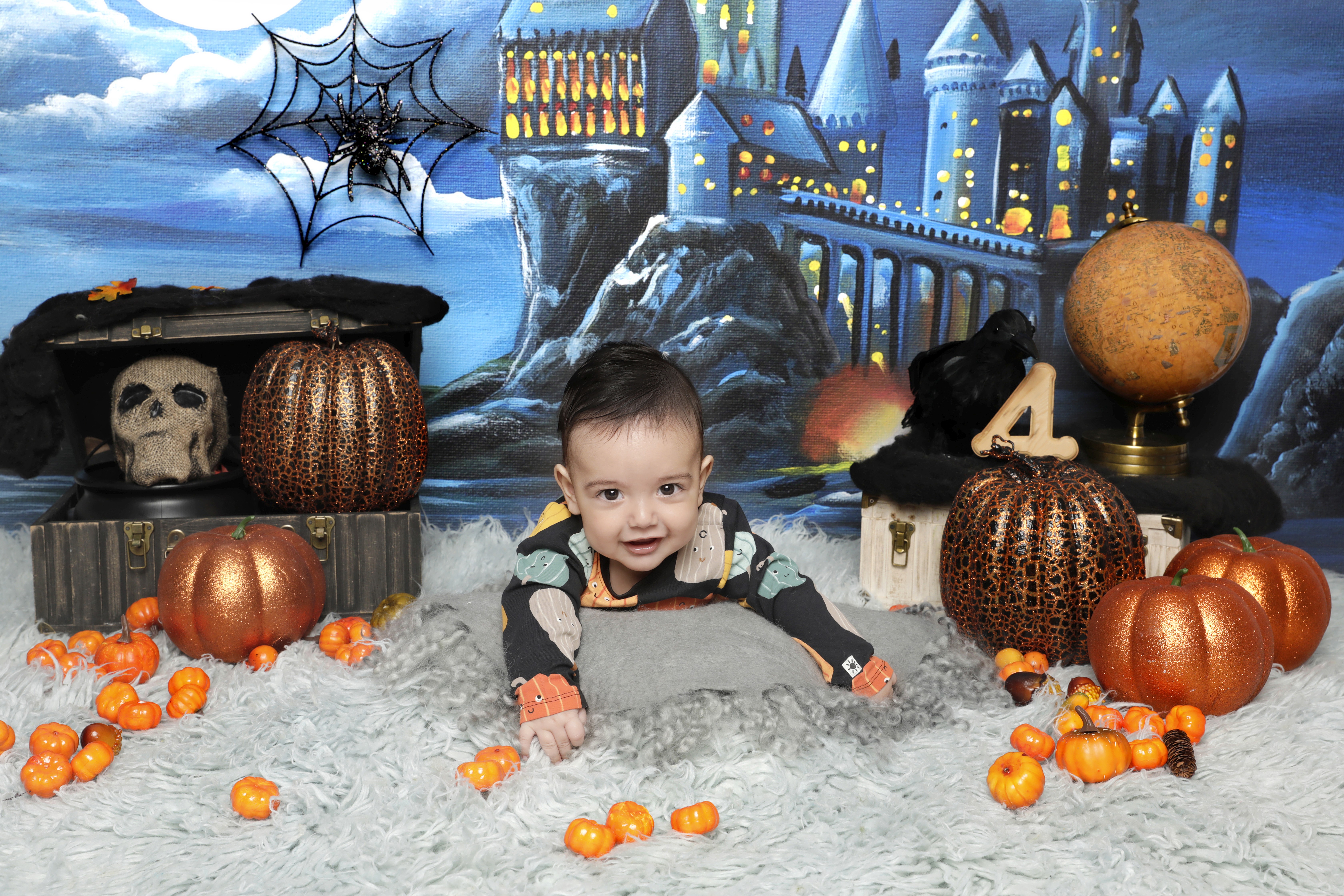 Baby boy in a Halloween-themed setup lying on his tummy.