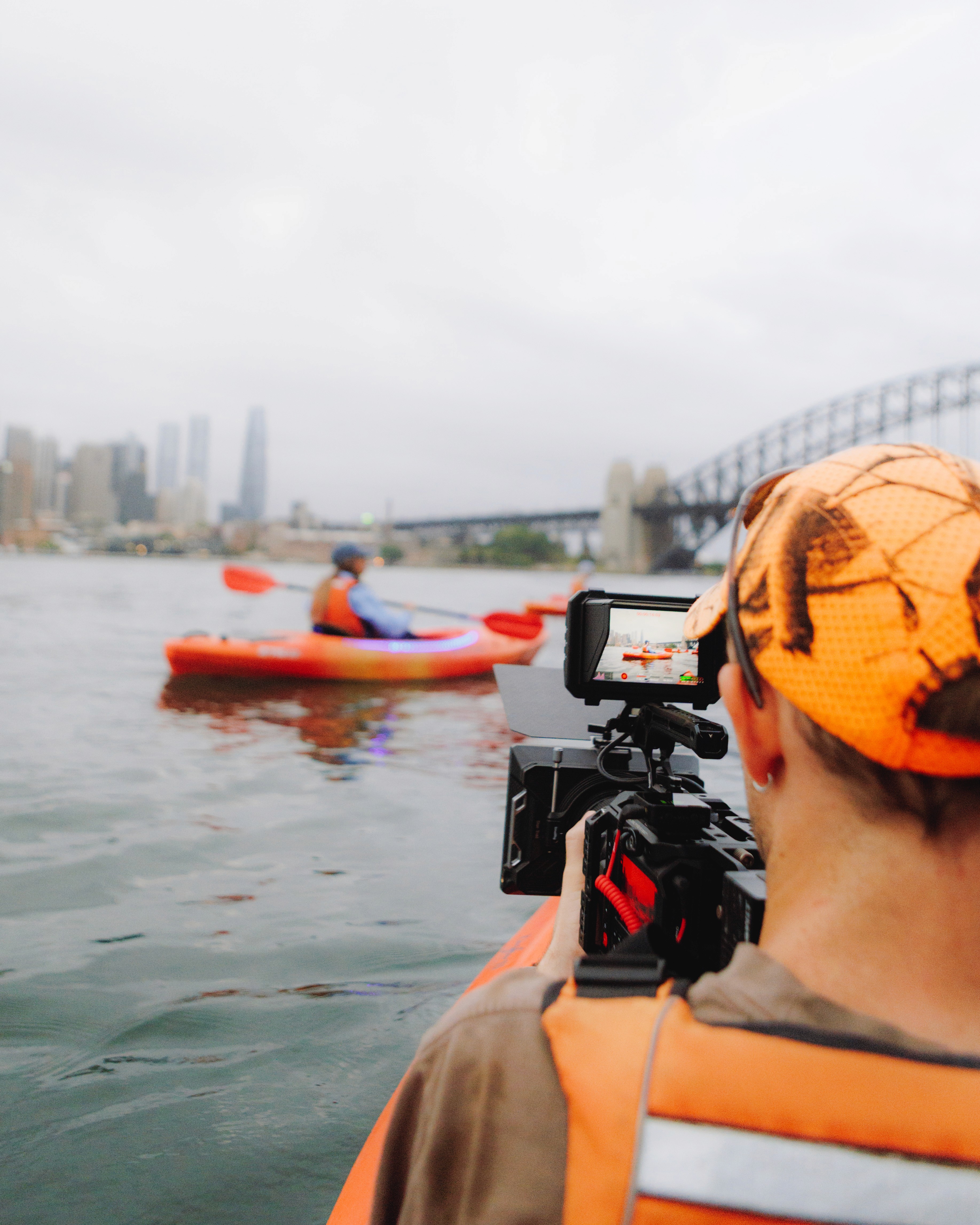 Behind the scenes of a cinema camer filming people kayaking under Sydney Harbour Bridge