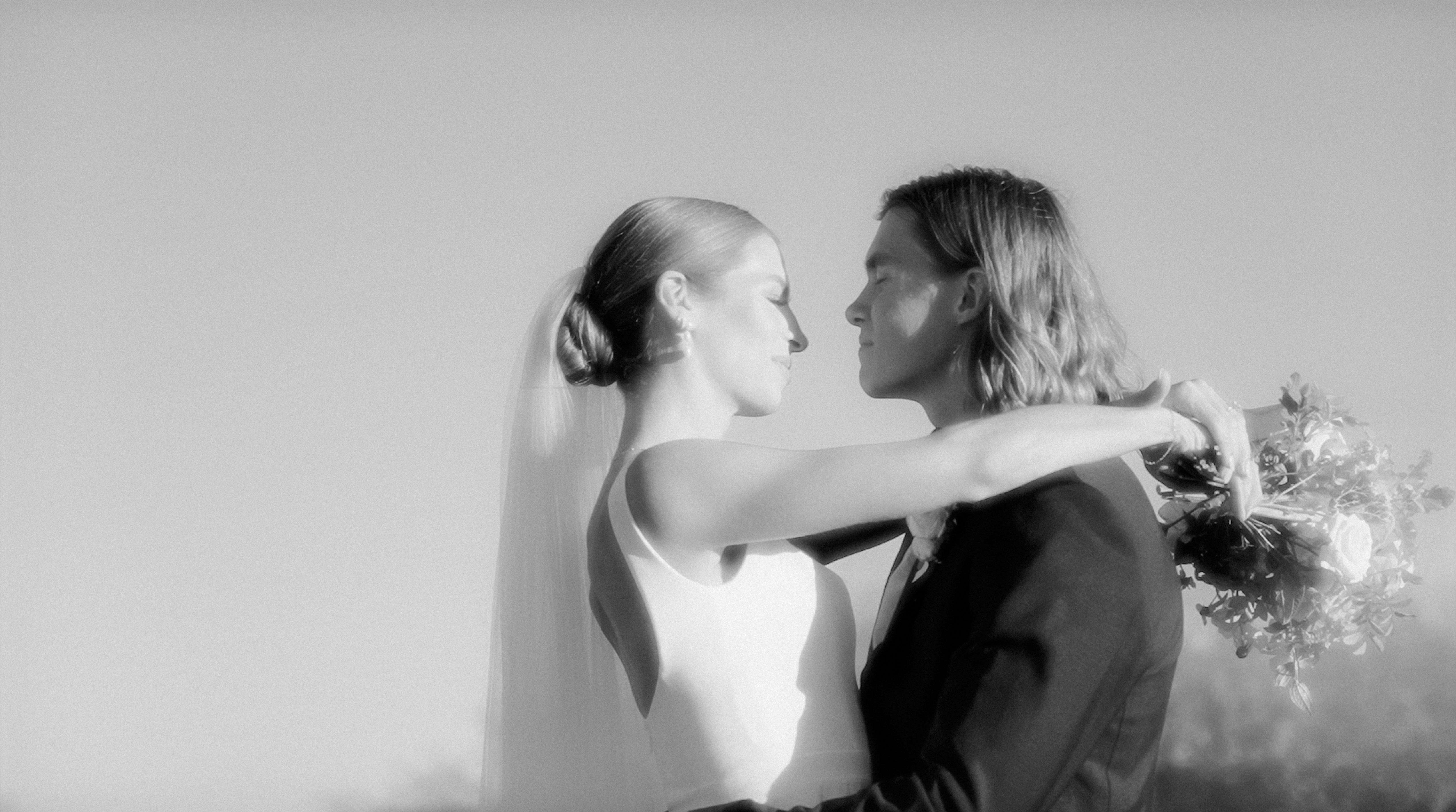 A couple embraces, gazing lovingly into each other's eyes, captured in black and white against a clear sky.