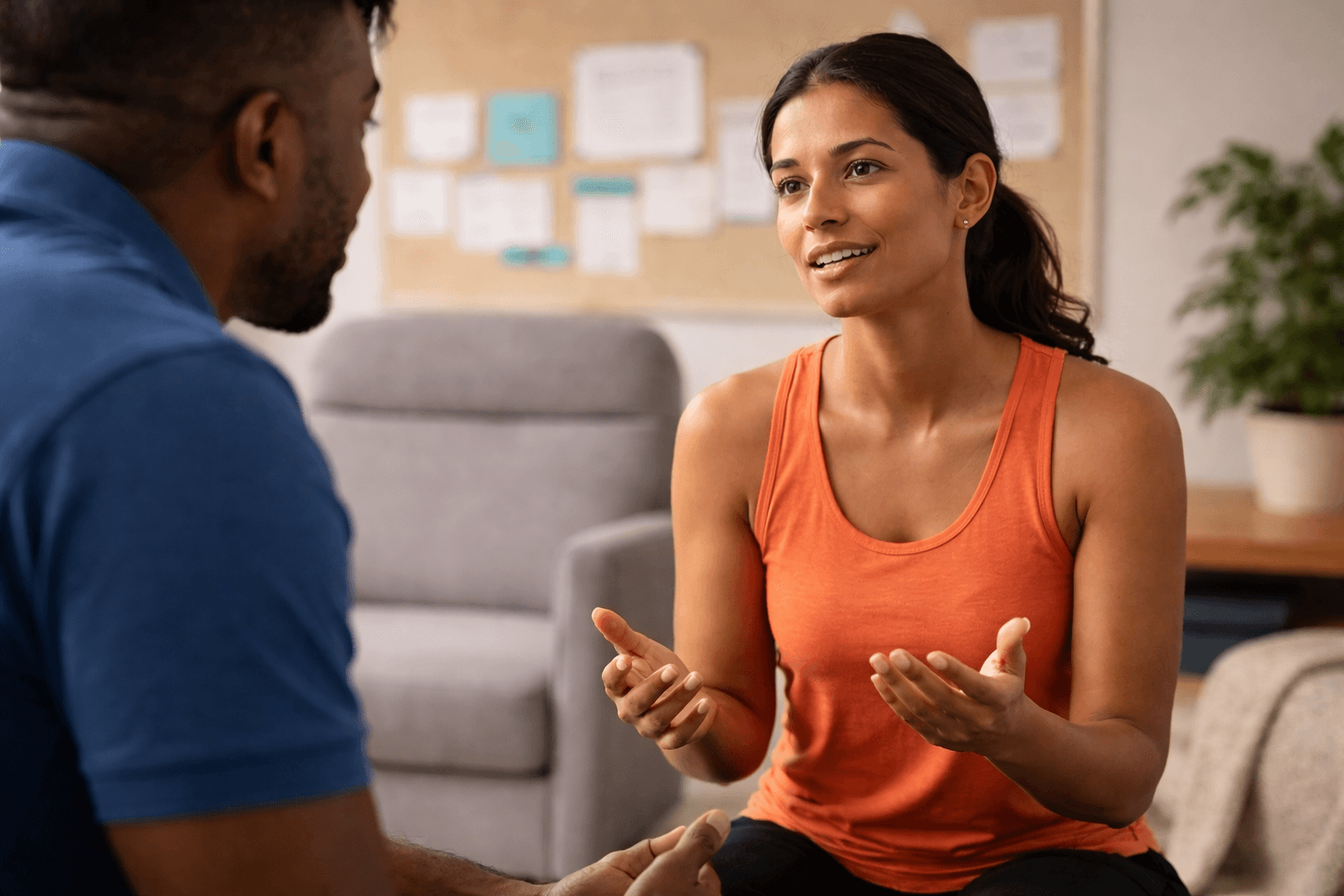 Patient in an orange top explaining her symptoms during a physical therapy consultation for chronic pain, while the physical therapist listens attentively.