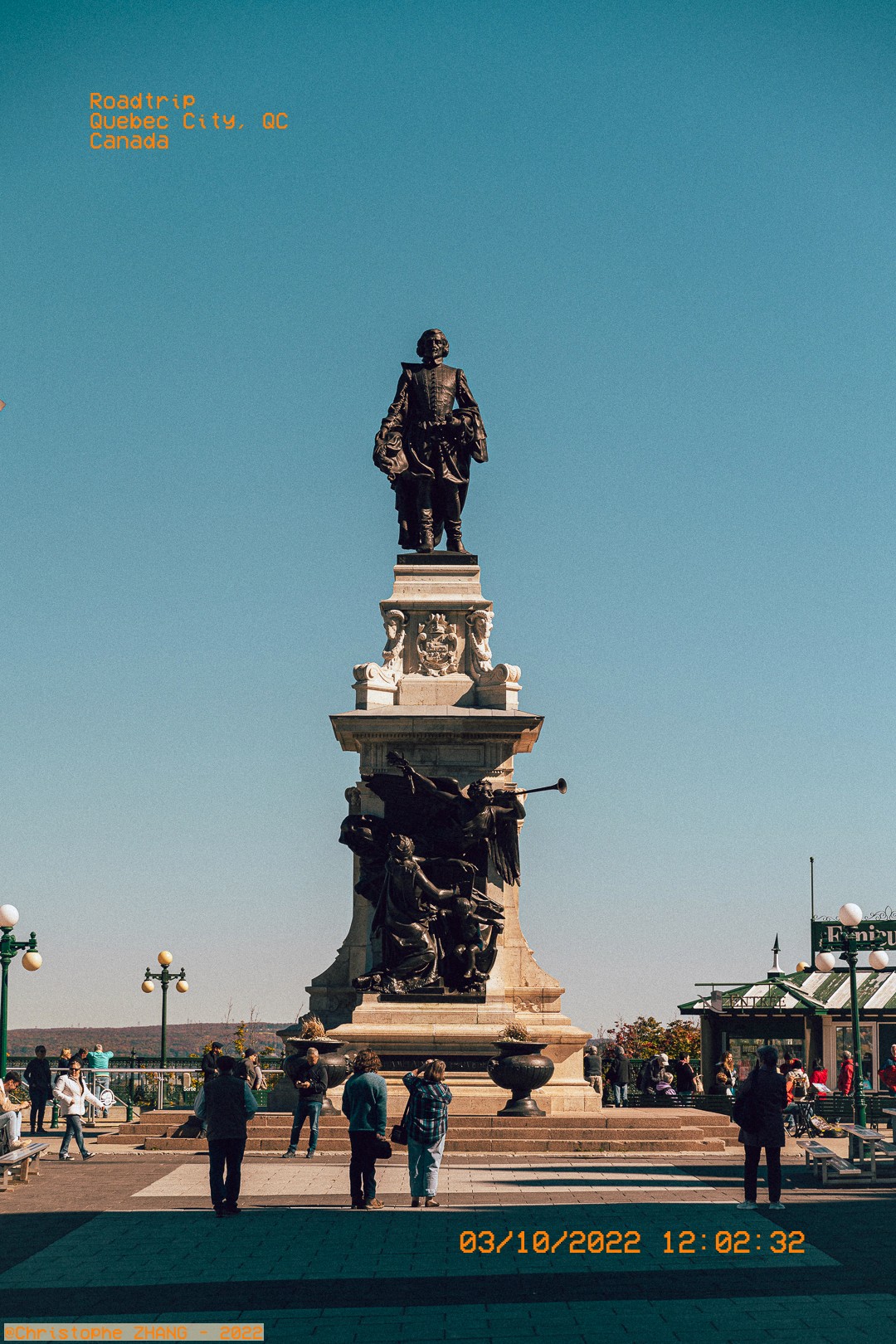 Statue de Samuel de Champlain à Québec, entourée de visiteurs sous un ciel bleu clair.
