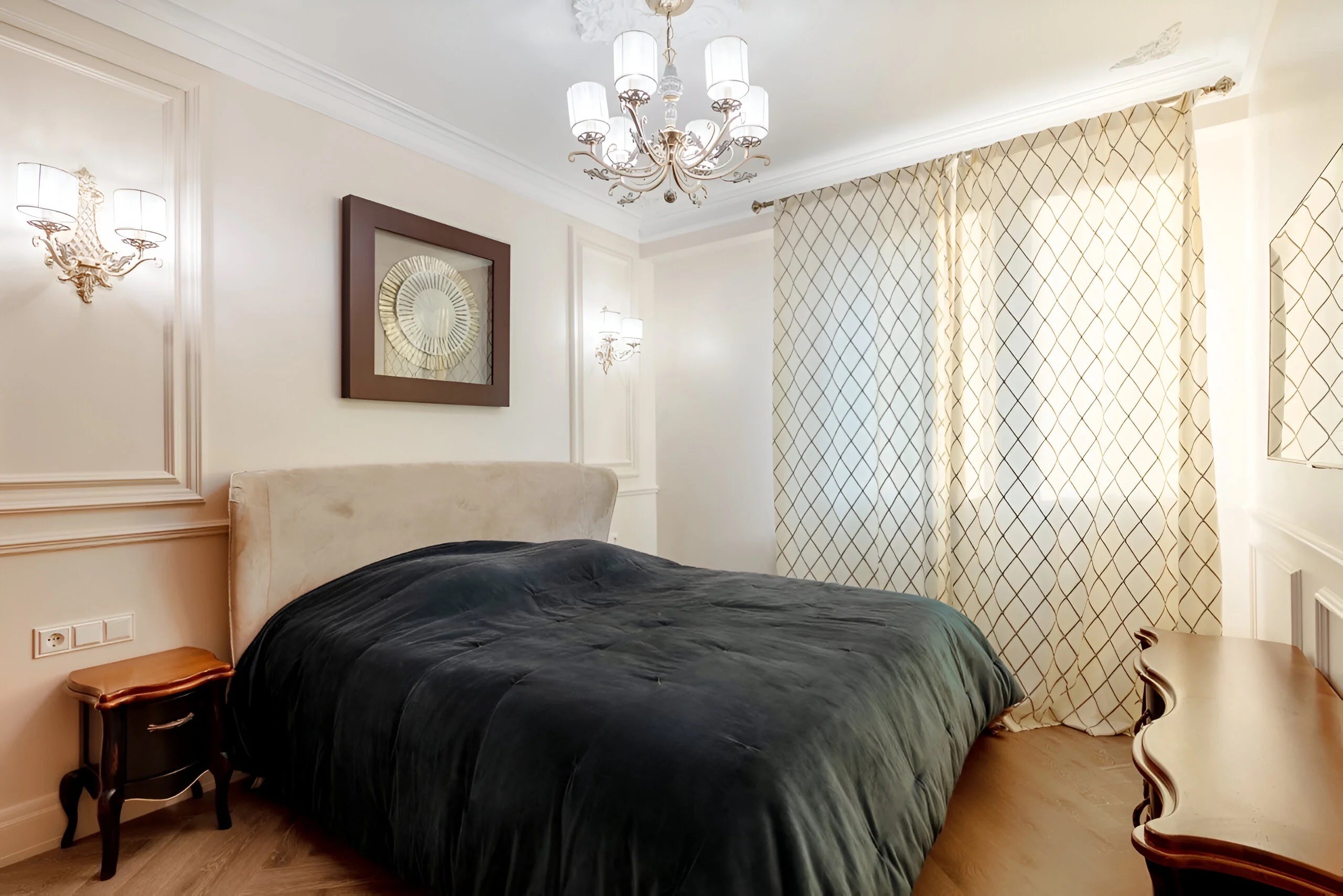 Chambre parentale luxueuse avec lustre en cristal, papier peint décoratif classique et literie noire contrastée.