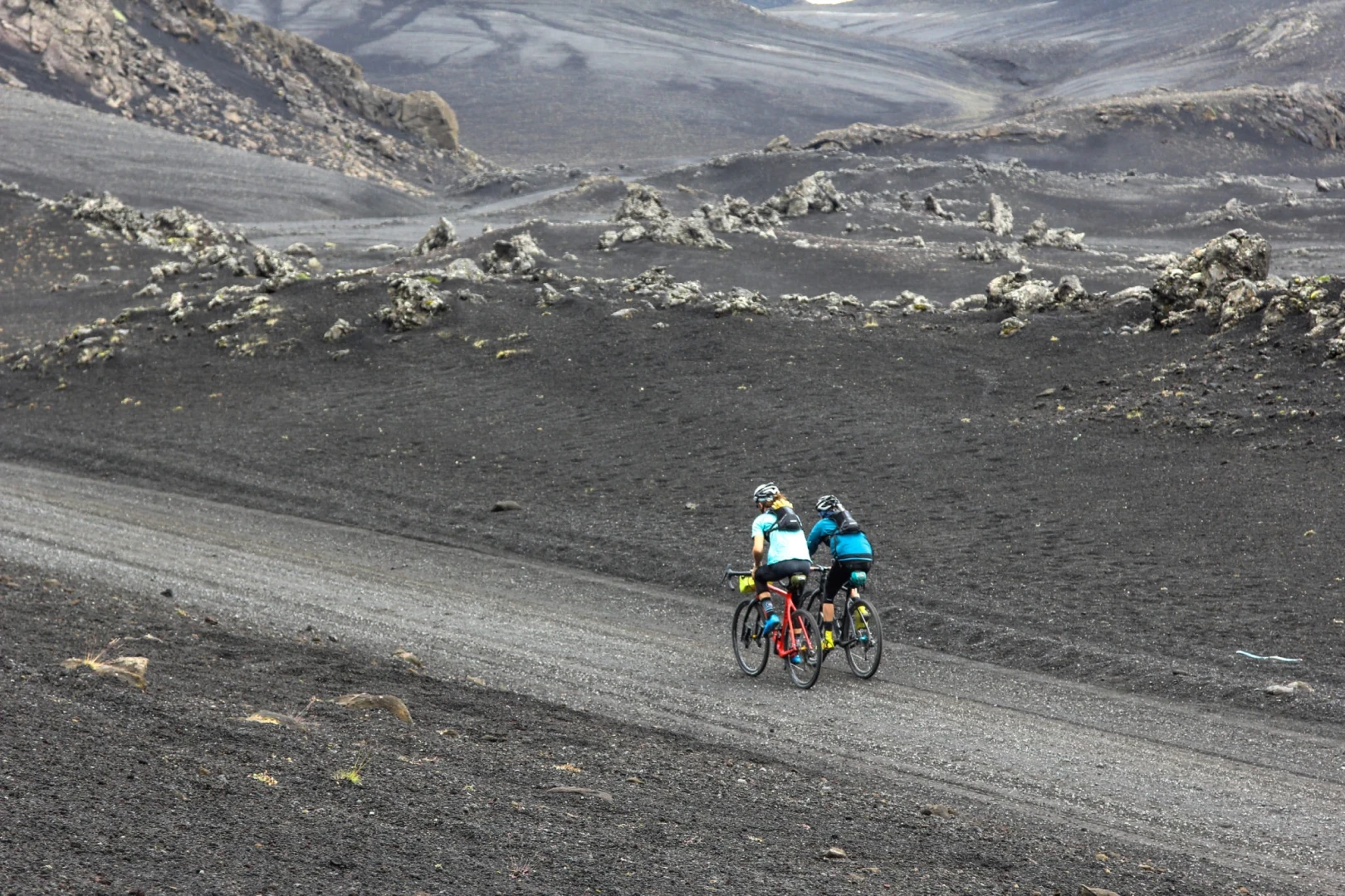 Man and woman pedal away from camera on a black sand moonscape road in Reykjanes