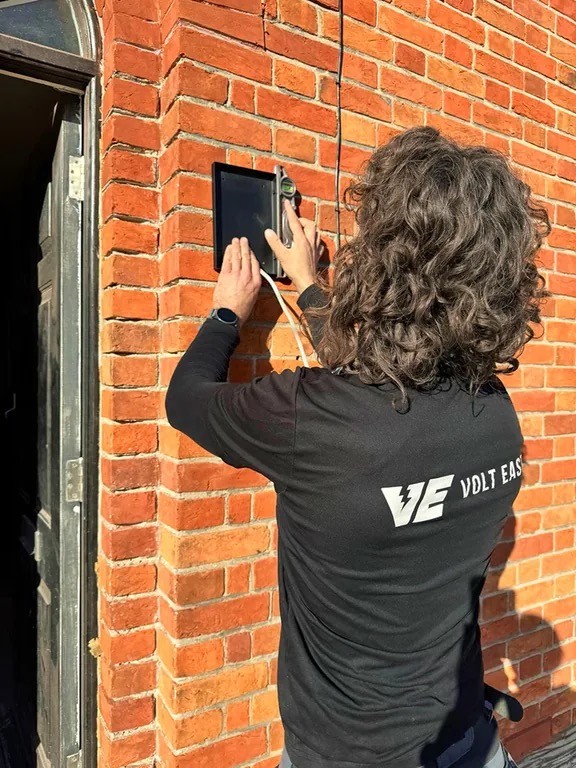 Volt East team member working on a wall-mounted device on a brick exterior during a Surrey security project