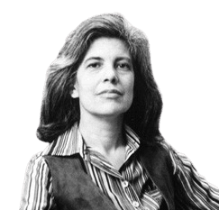 A black-and-white portrait of a confident woman with voluminous hair, wearing a striped shirt and a vest, sitting in front of a bookshelf filled with books. The image captures a scholarly and intellectual atmosphere, emphasizing her poised demeanor and thoughtful expression.