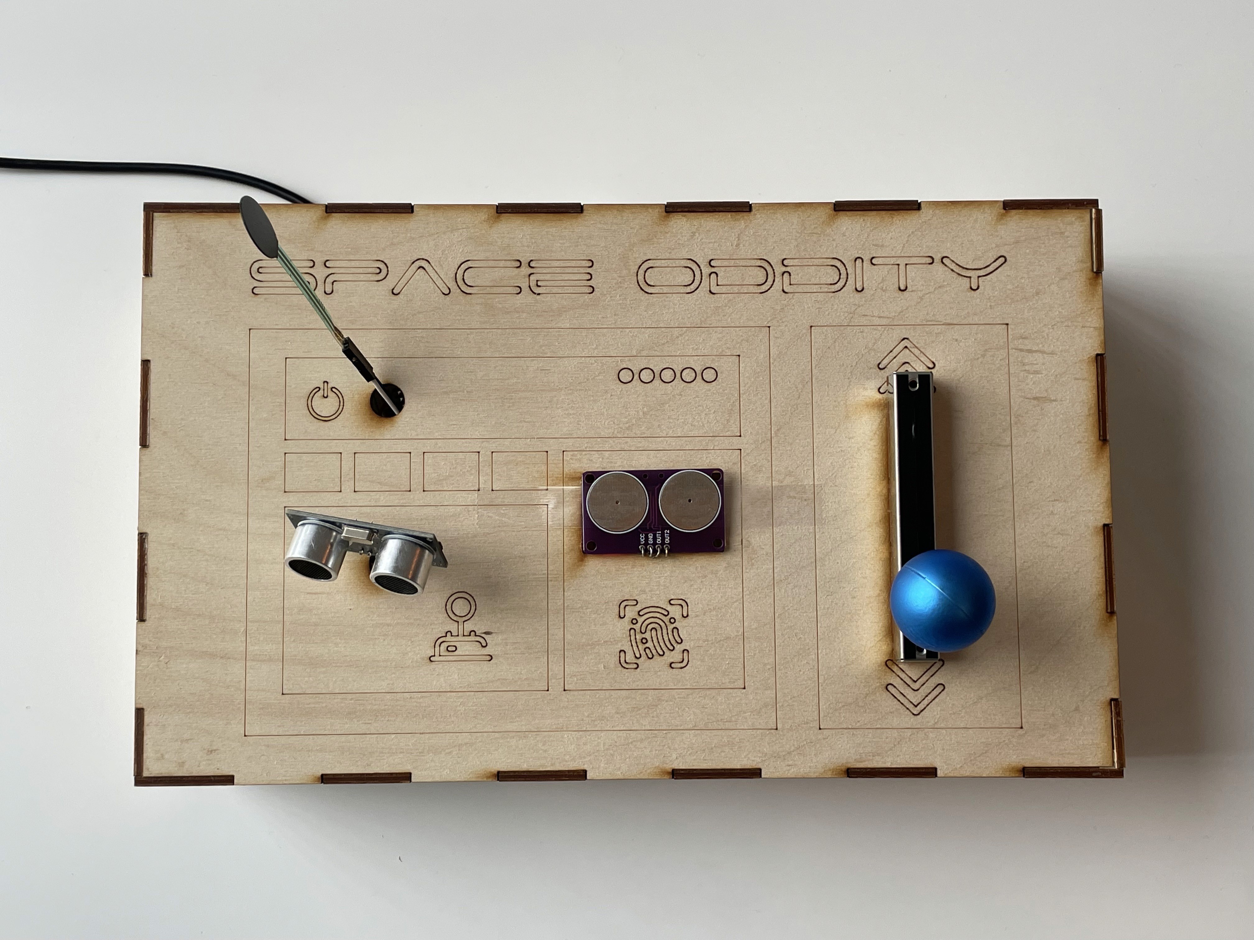 Laser-cut wooden control box with switches, knobs, a joystick, and engraved interface labels.